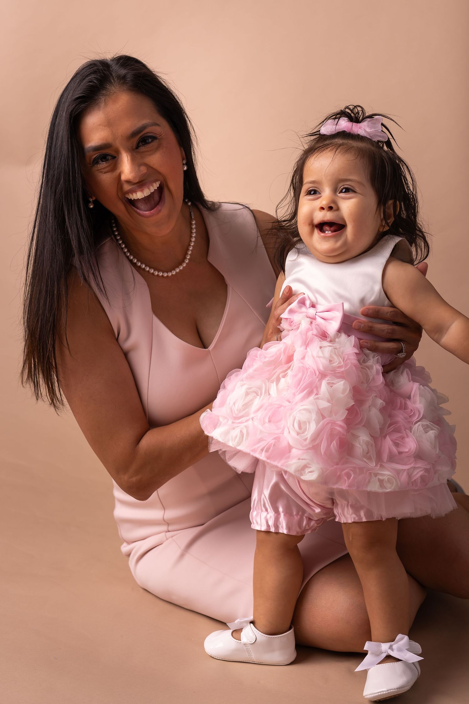 Mother and daughter in matching pink outfits share joyful moments during a first birthday photoshoot.
