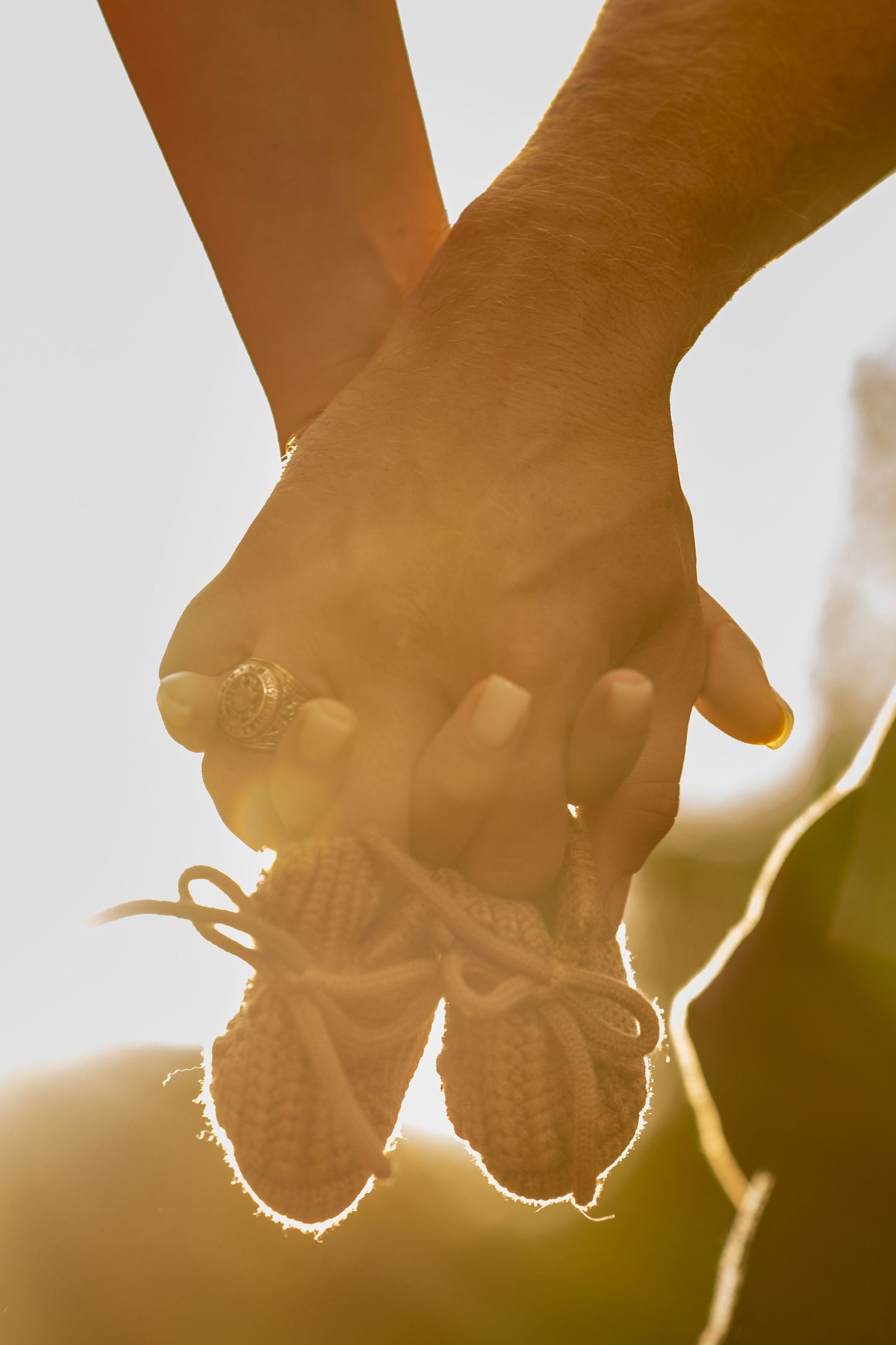 Two hands holding tiny knitted baby booties together in warm golden sunlight, symbolizing love and new parenthood.
