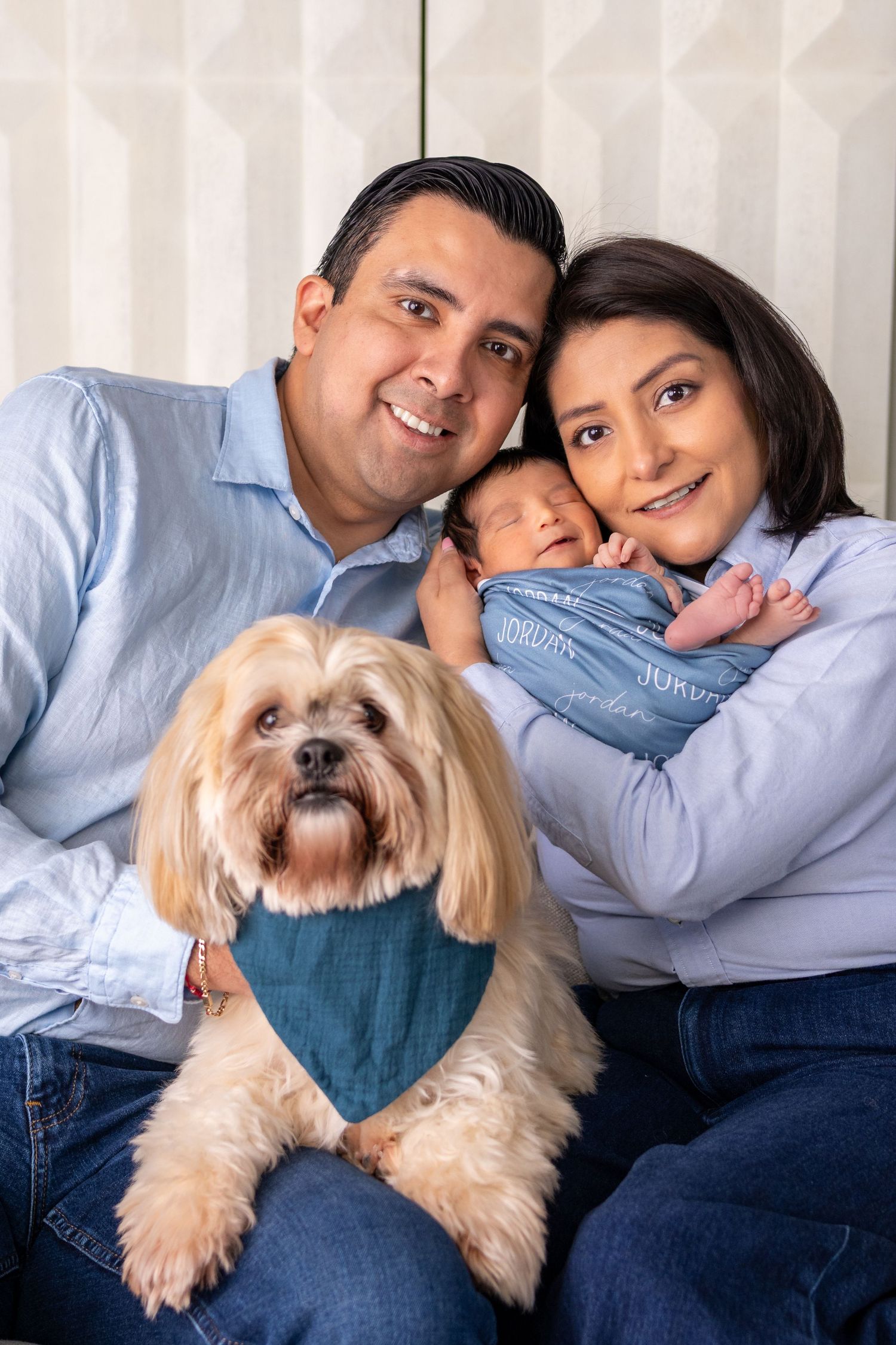 Happy couple with newborn baby and fluffy Shih Tzu dog wearing a teal bandana in a family portrait.