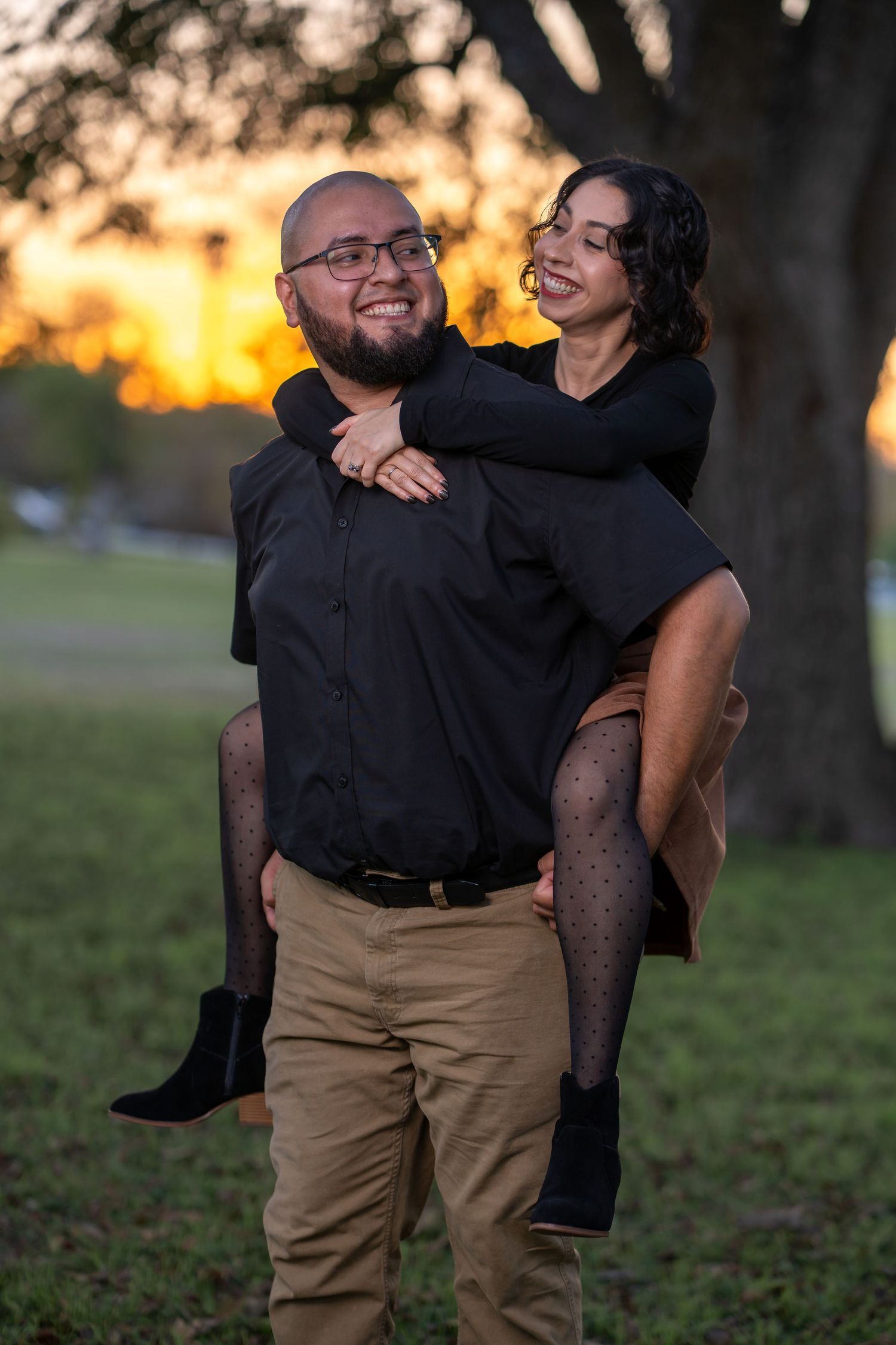 A couple shares a joyful moment together during sunset in a park, with one person giving the other a piggyback ride.