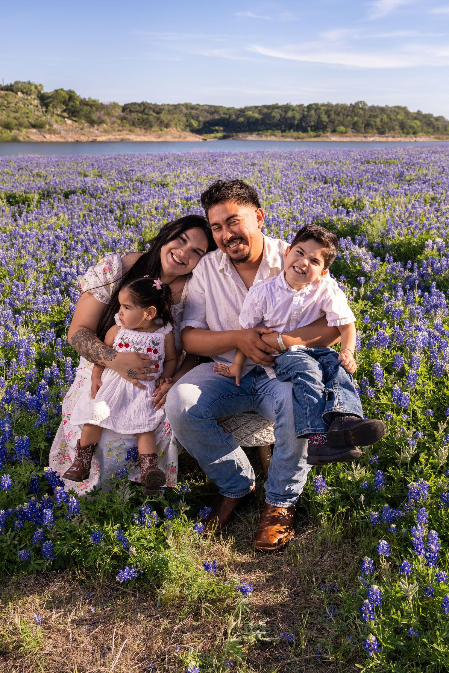 Happy family of four sitting in a field of Texas bluebonnets under a blue sky.