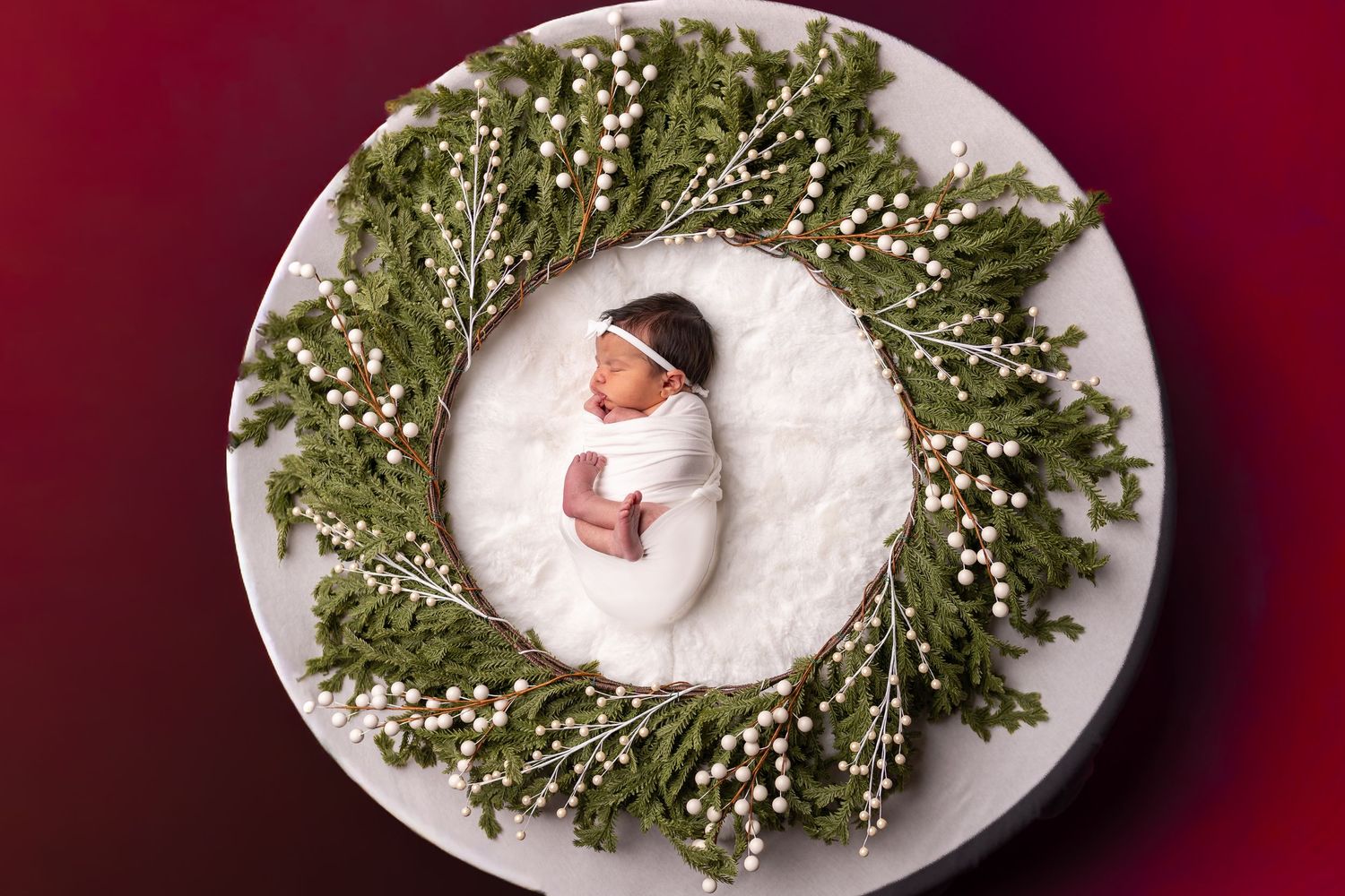 Holiday wreath decorations with white berries and greenery arranged on white plates against a deep red background.