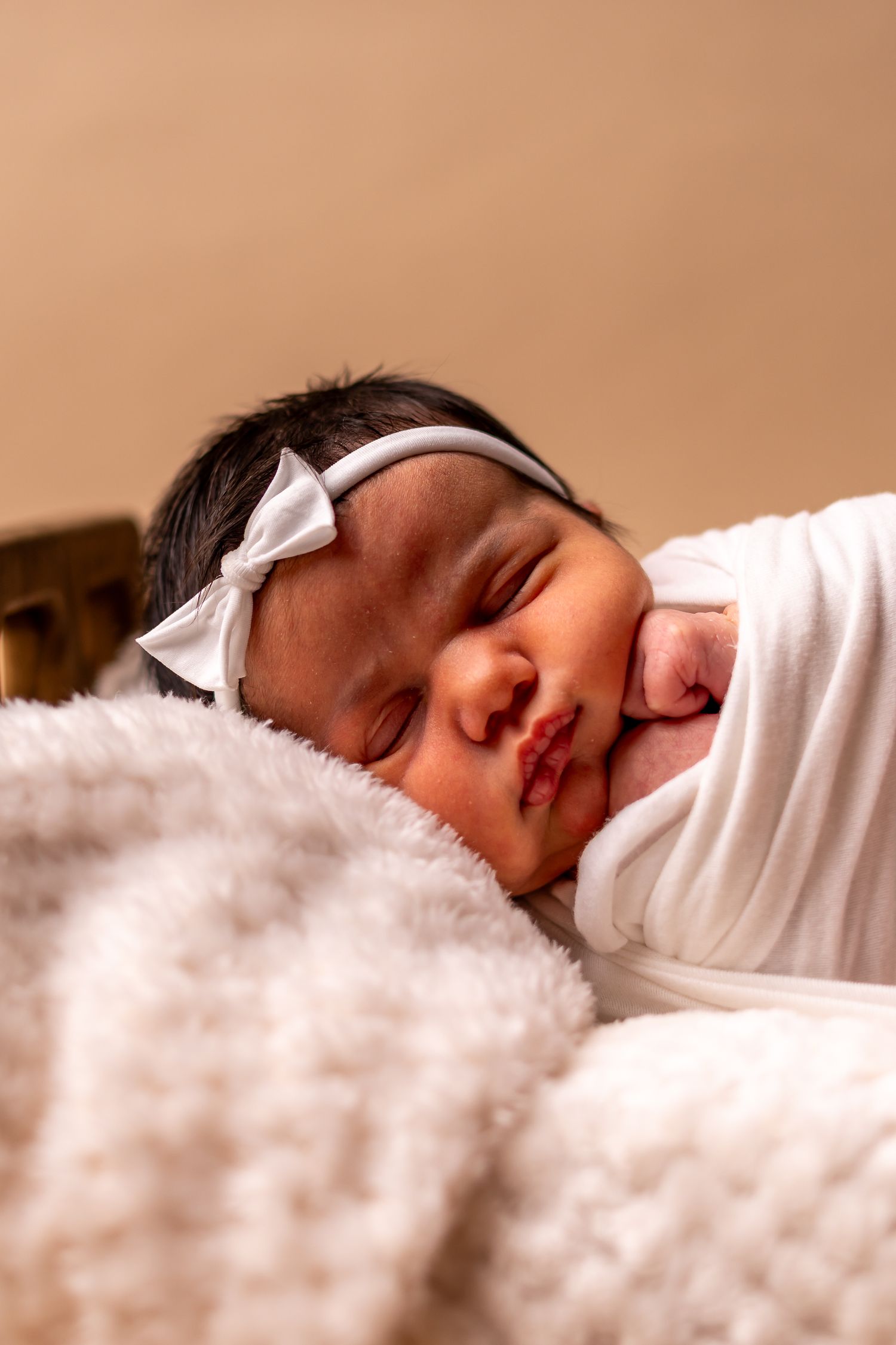 A sleeping newborn baby lies peacefully on soft white fluffy blankets in a series of connected photos.
