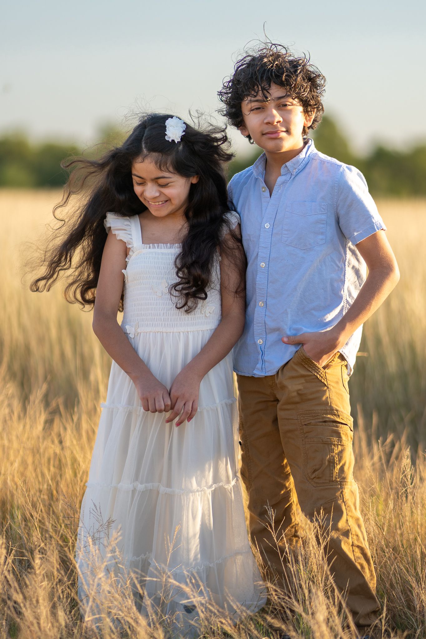 Two children playing together in tall grass during golden hour.