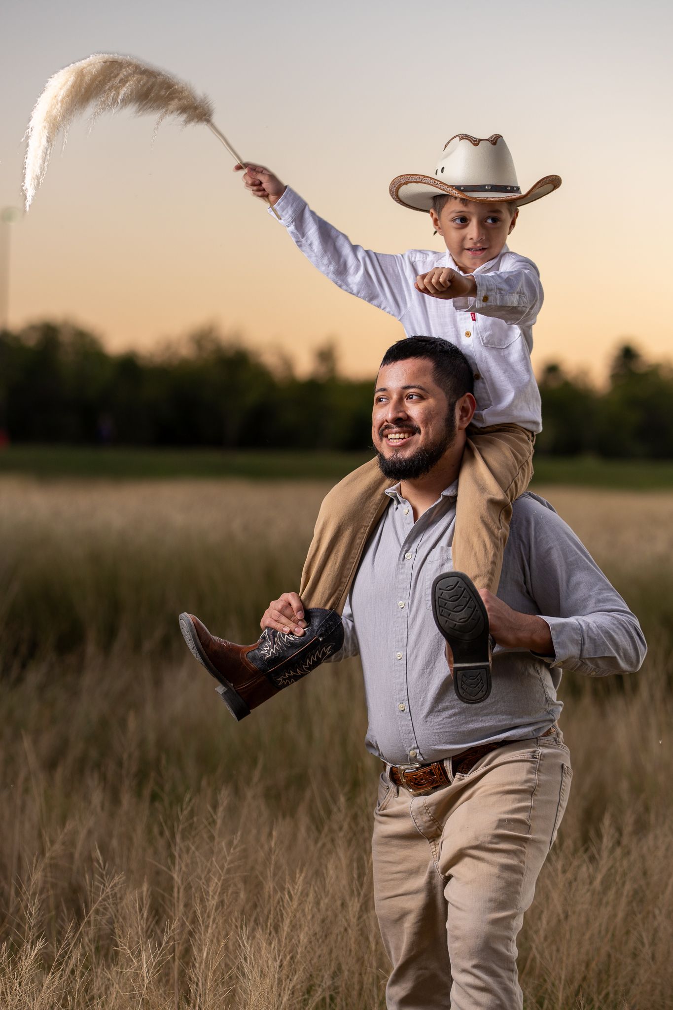 Playful family moment captured in a rustic field at sunset.