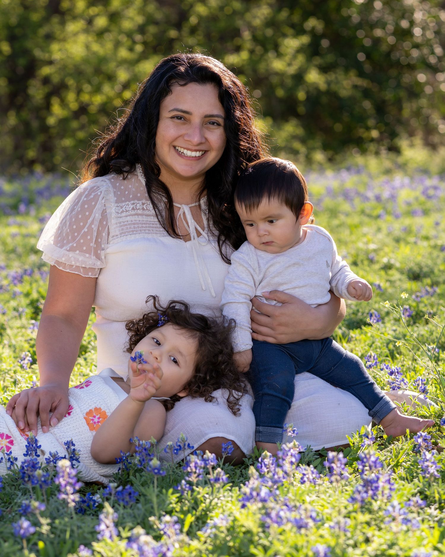 A family sits together in a blooming field of bluebonnets on a sunny spring day.