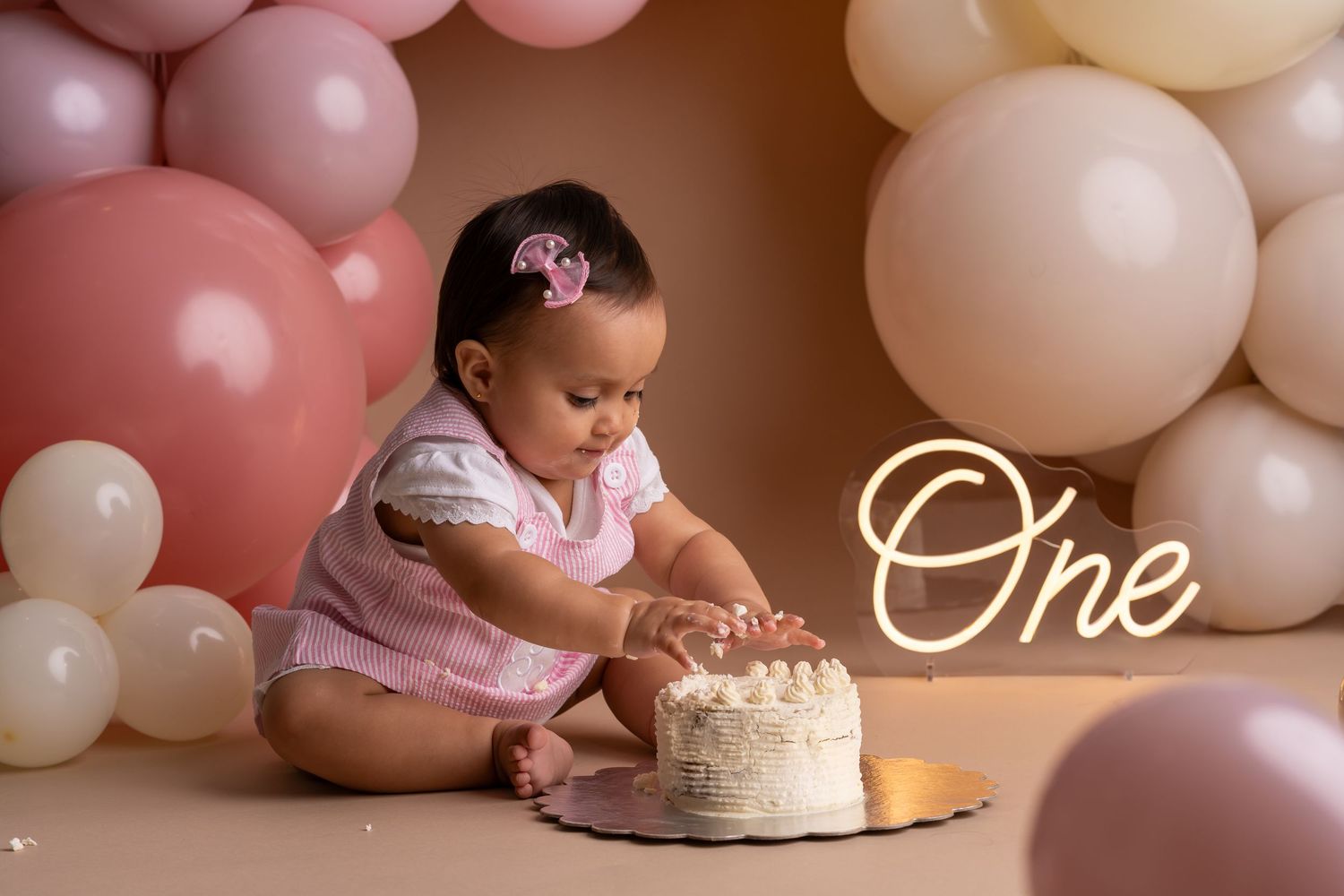 A cake smash photo session with pastel pink and beige balloon decorations for a first birthday celebration.
