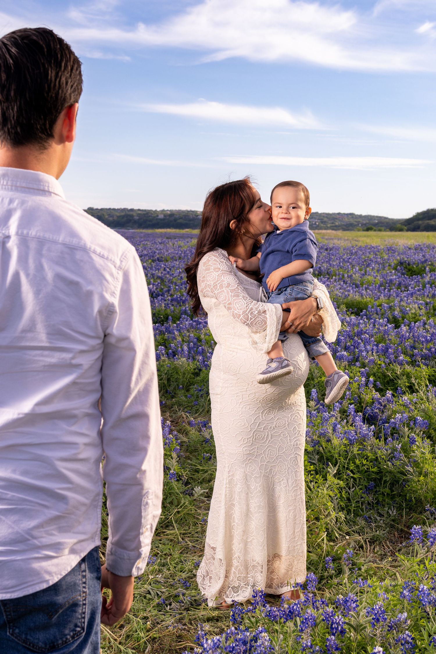 Family photo session in a Texas bluebonnet field with a mother kissing her baby while father watches.