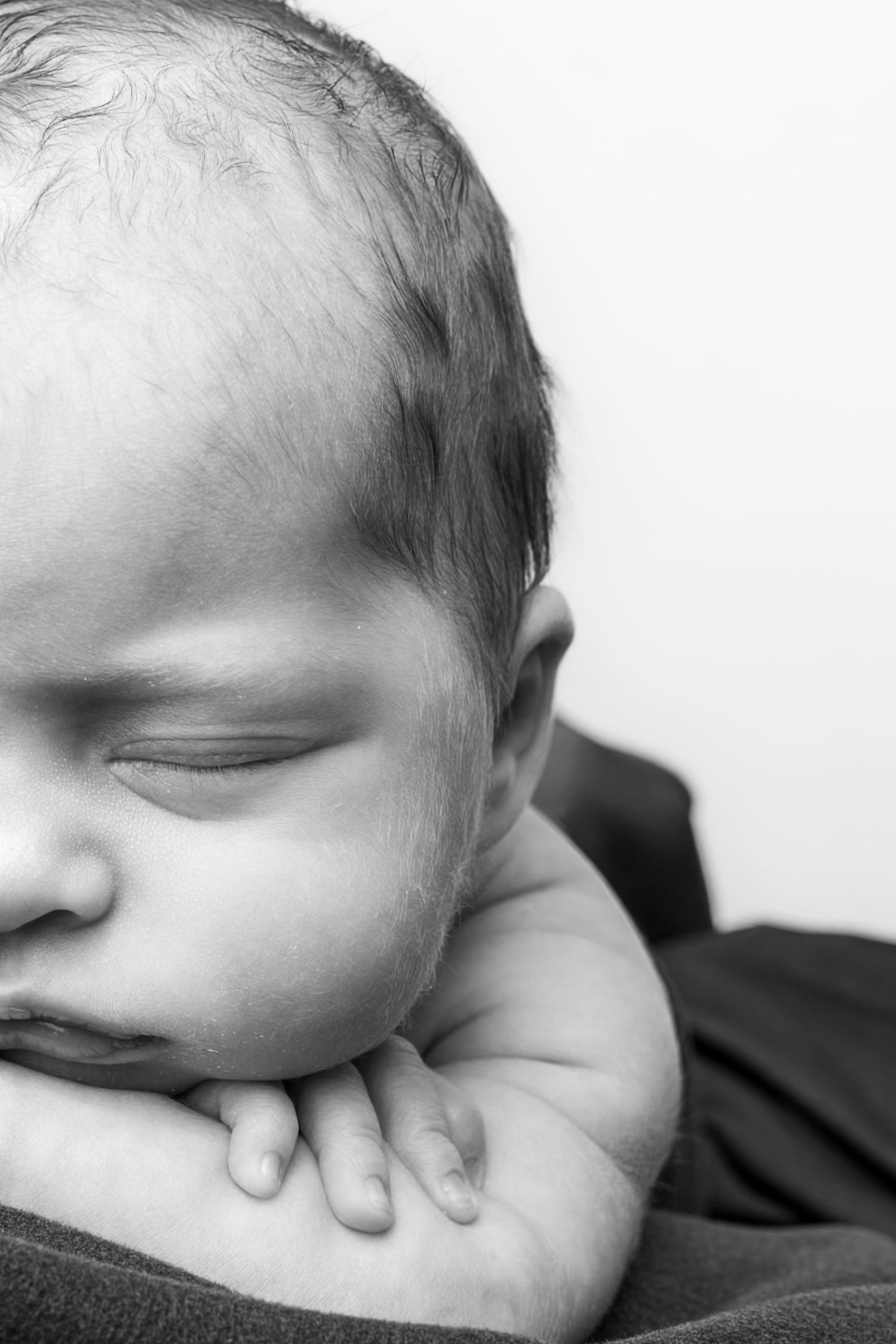 Black and white close-up portrait of a sleeping newborn baby resting chin on tiny hands.