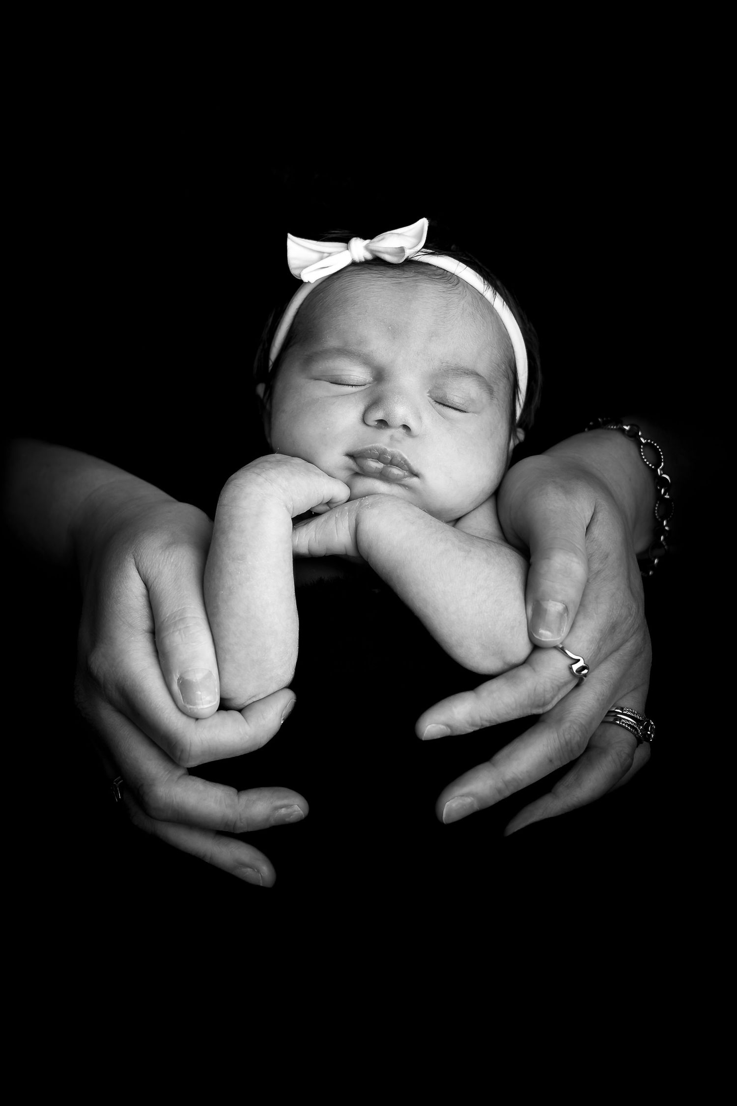 A black and white photo showing a sleeping baby cradled in gentle hands against a dark background.