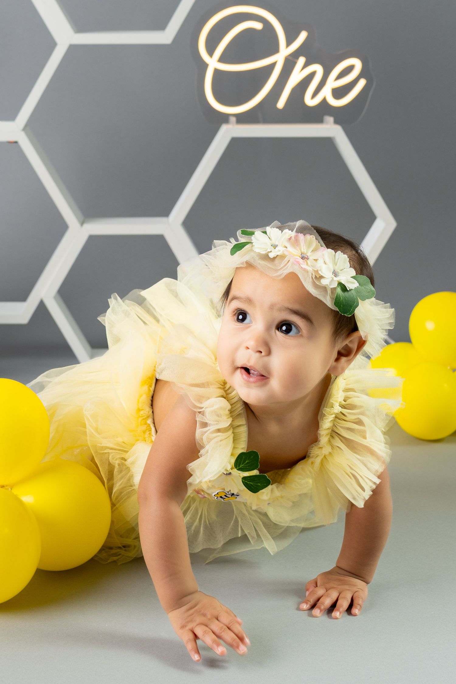 Adorable baby girl in yellow tutu crawls among balloons at her first birthday photo session.