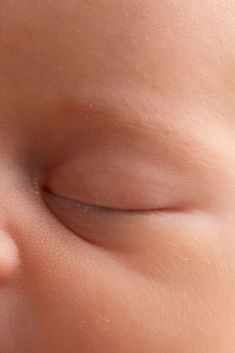 Close-up macro photo of a sleeping newborn baby's closed eye with delicate eyelashes and soft skin.