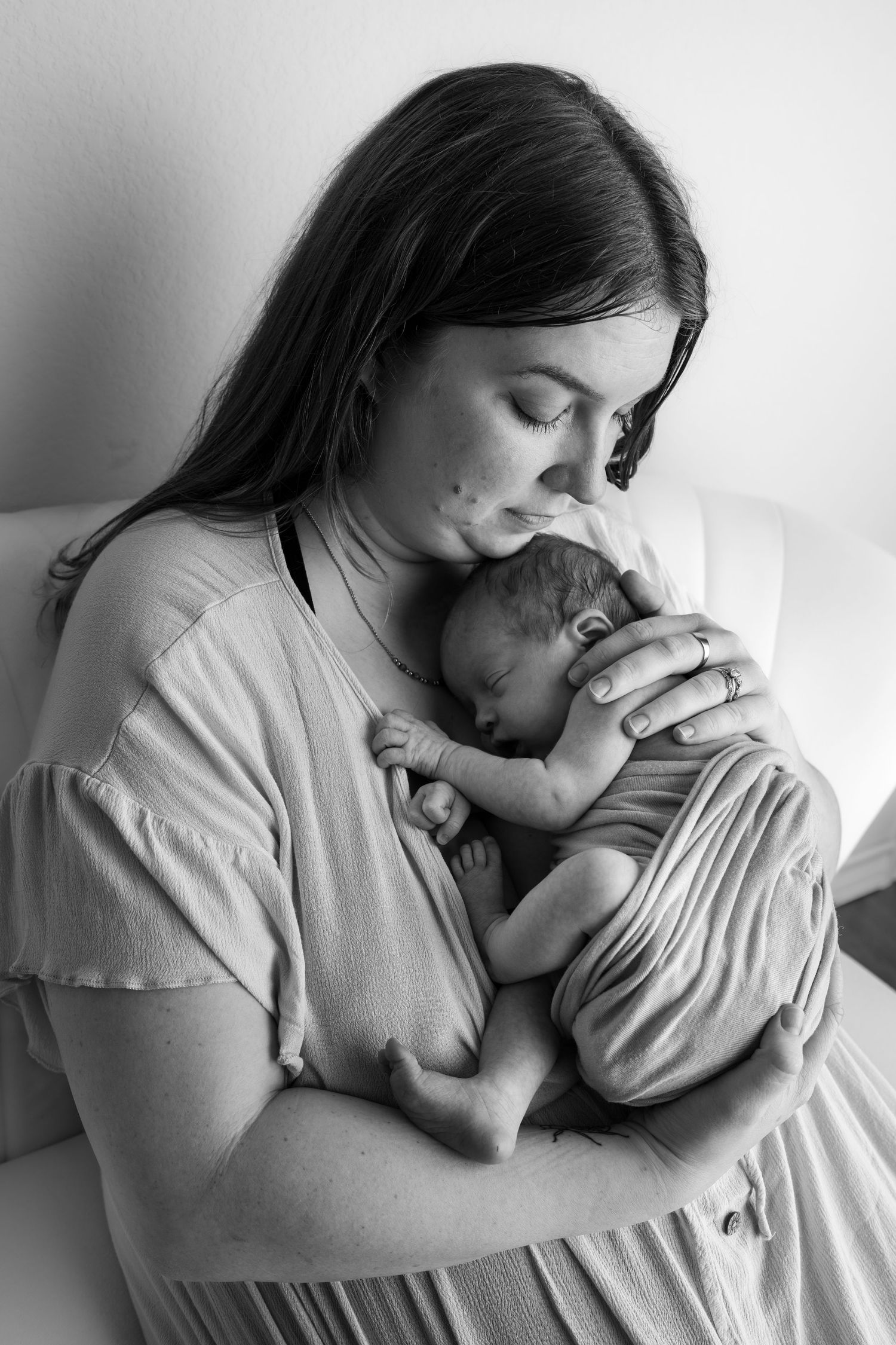 Black and white photo of a mother tenderly kissing her sleeping newborn baby while cradling them close.