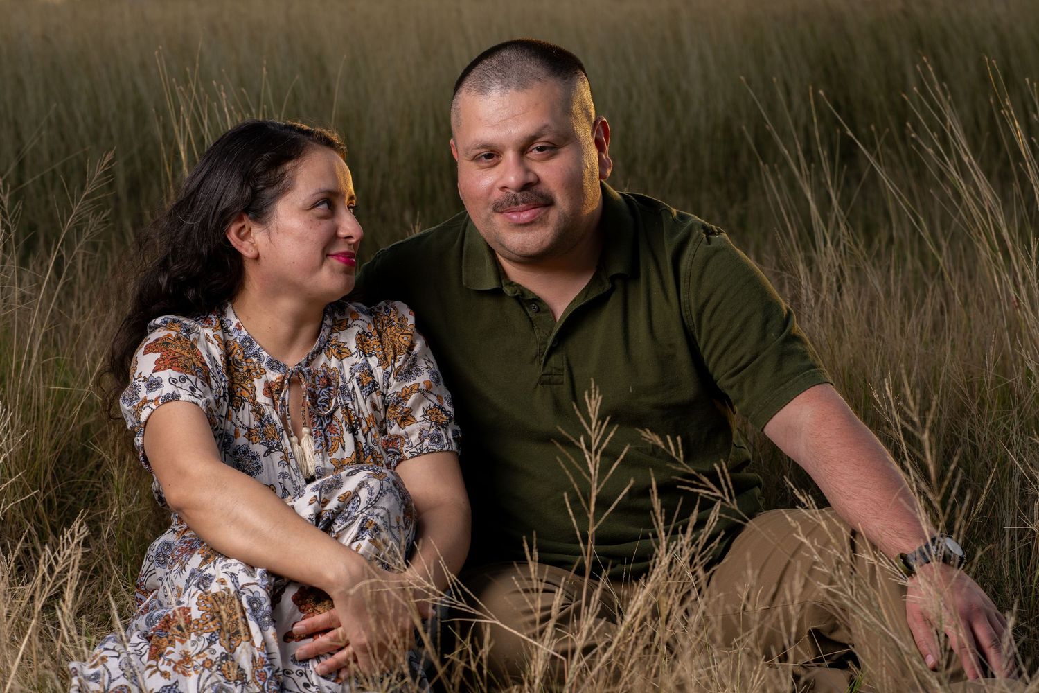 A couple sits together in a field of tall grass during a romantic outdoor photo session.