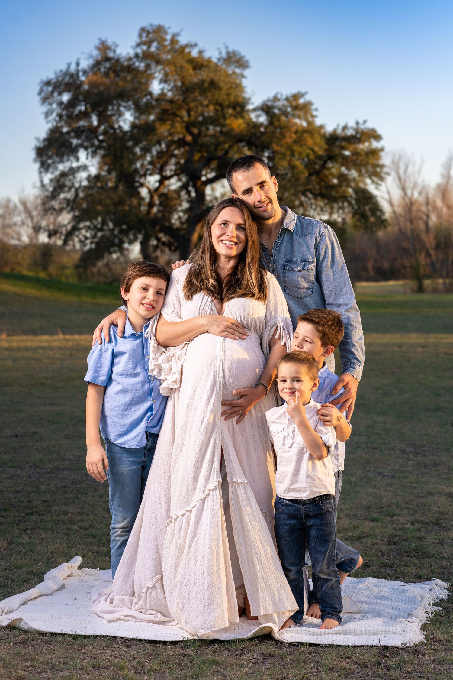 Family sitting together on a white blanket in a grassy field during golden hour.