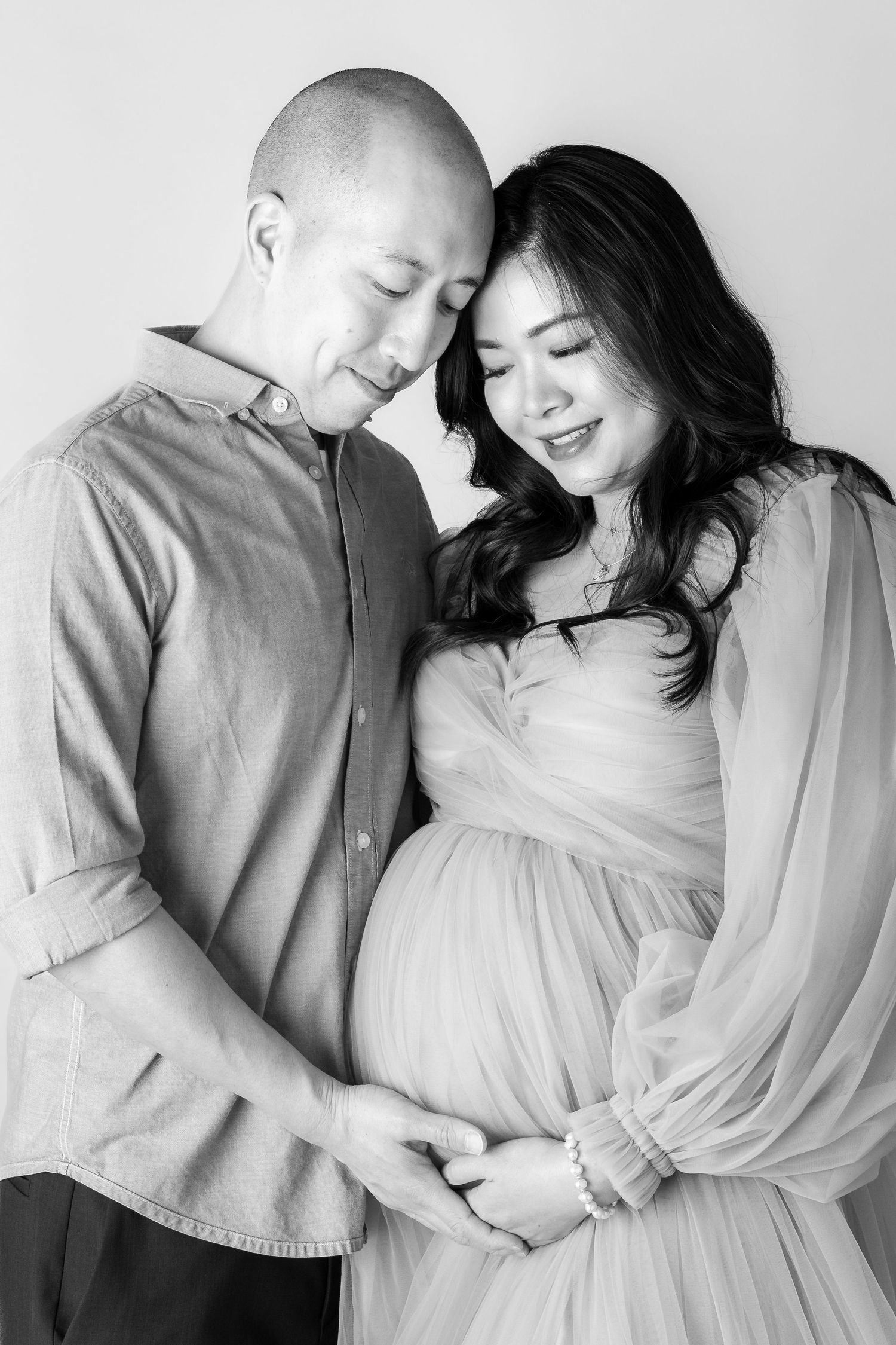 Black and white maternity photo of a couple tenderly holding the pregnant woman's baby bump in a studio setting.