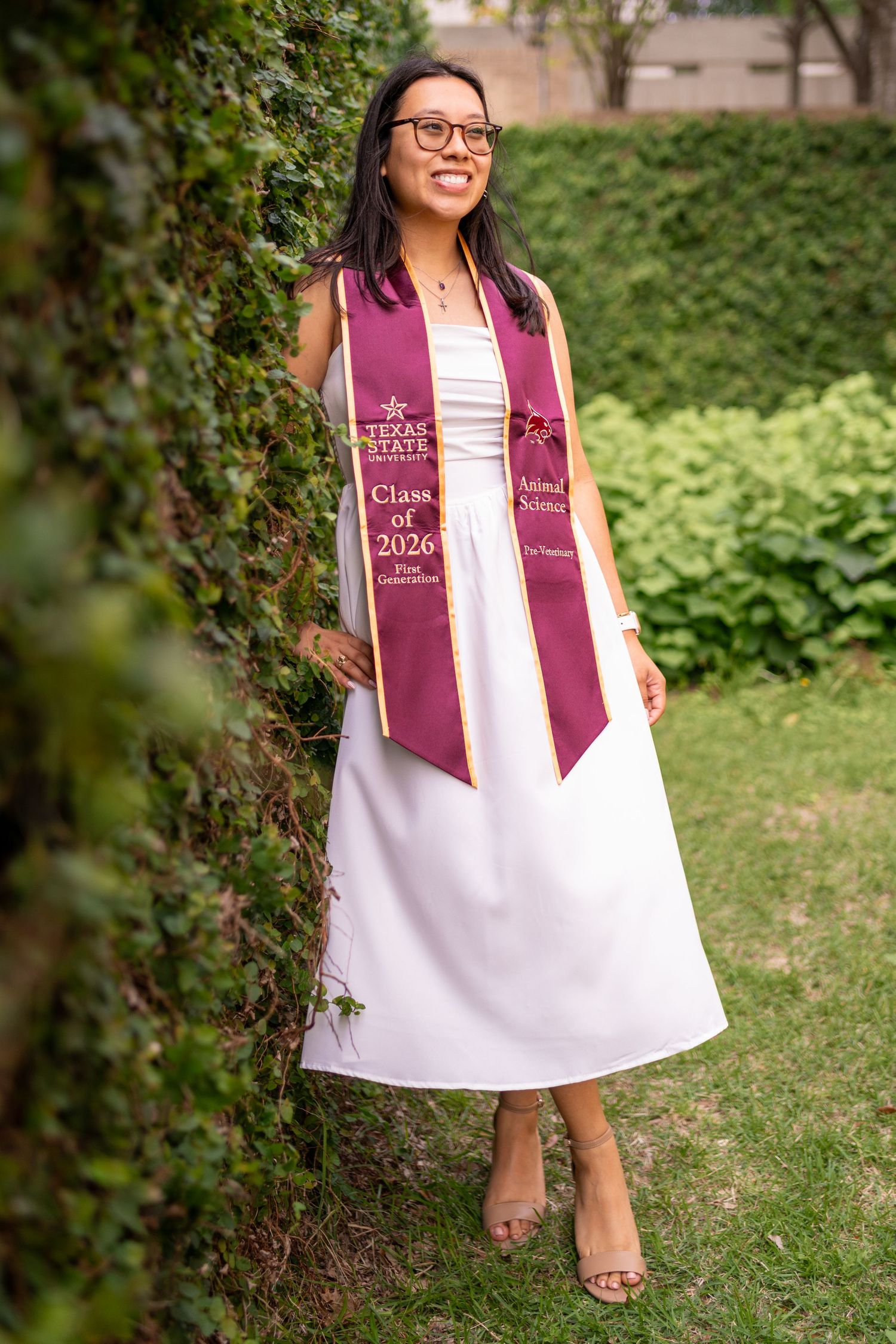 Texas State University Class of 2026 Animal Science graduate smiling in white dress with maroon stole outdoors.