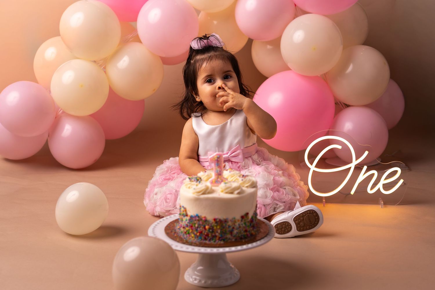 Pink and white balloons create a festive backdrop for a birthday celebration with cake and decorations.
