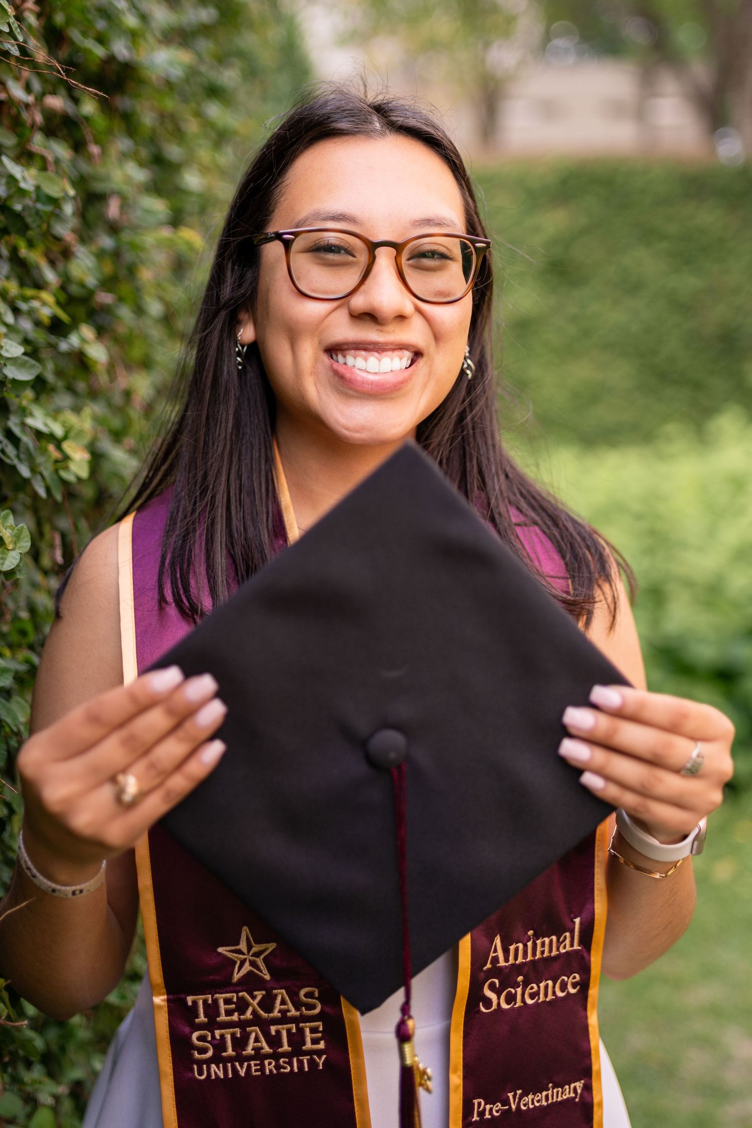 Texas State University Animal Science Pre-Veterinary graduate smiling and holding her black graduation cap outdoors.
