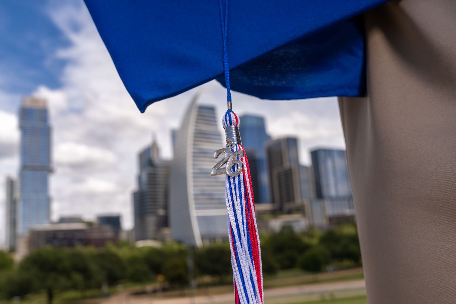 Close-up of blue graduation cap tassel with red white blue ribbons against city skyline backdrop.