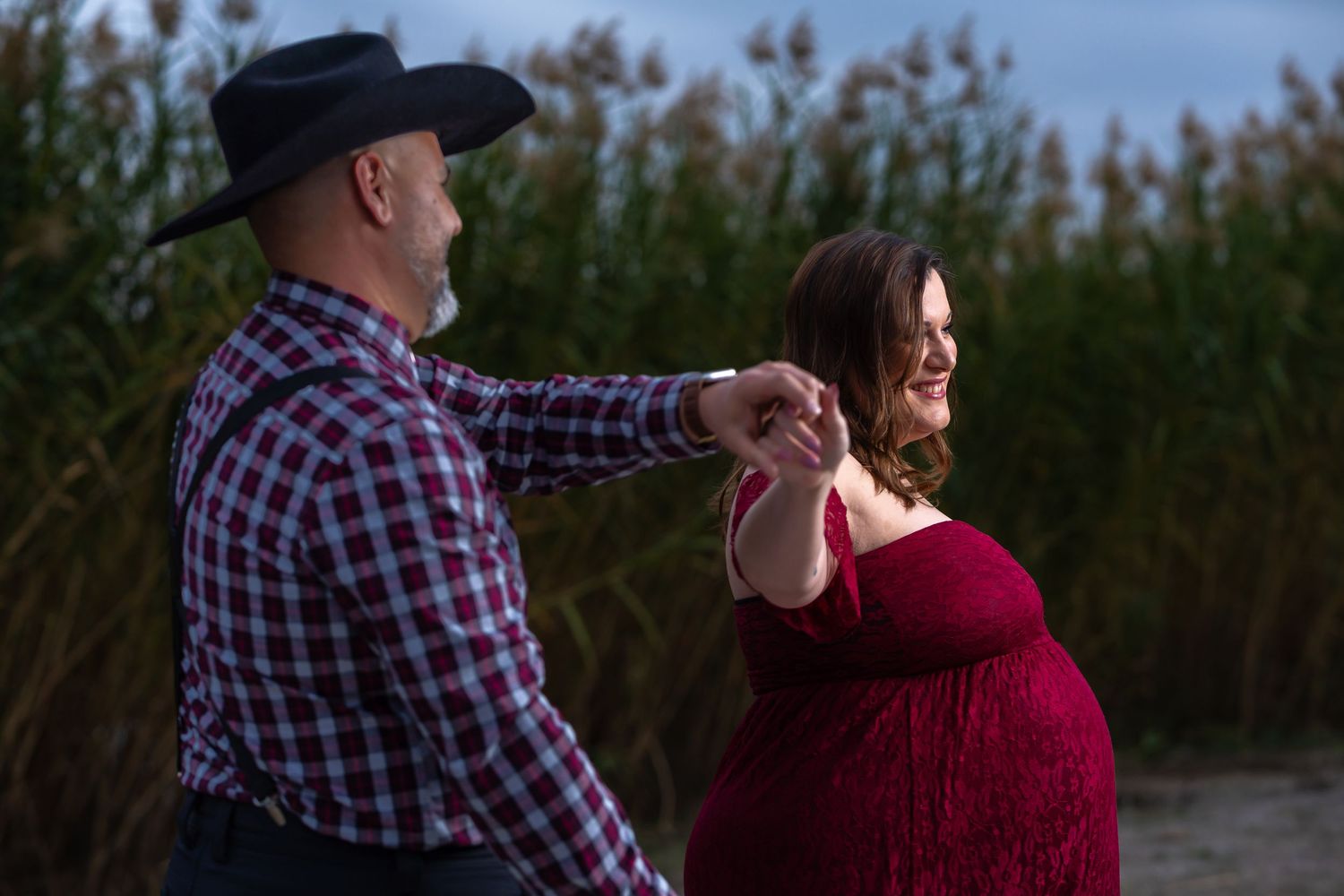 A couple in casual attire dances together in front of a natural outdoor backdrop at sunset.