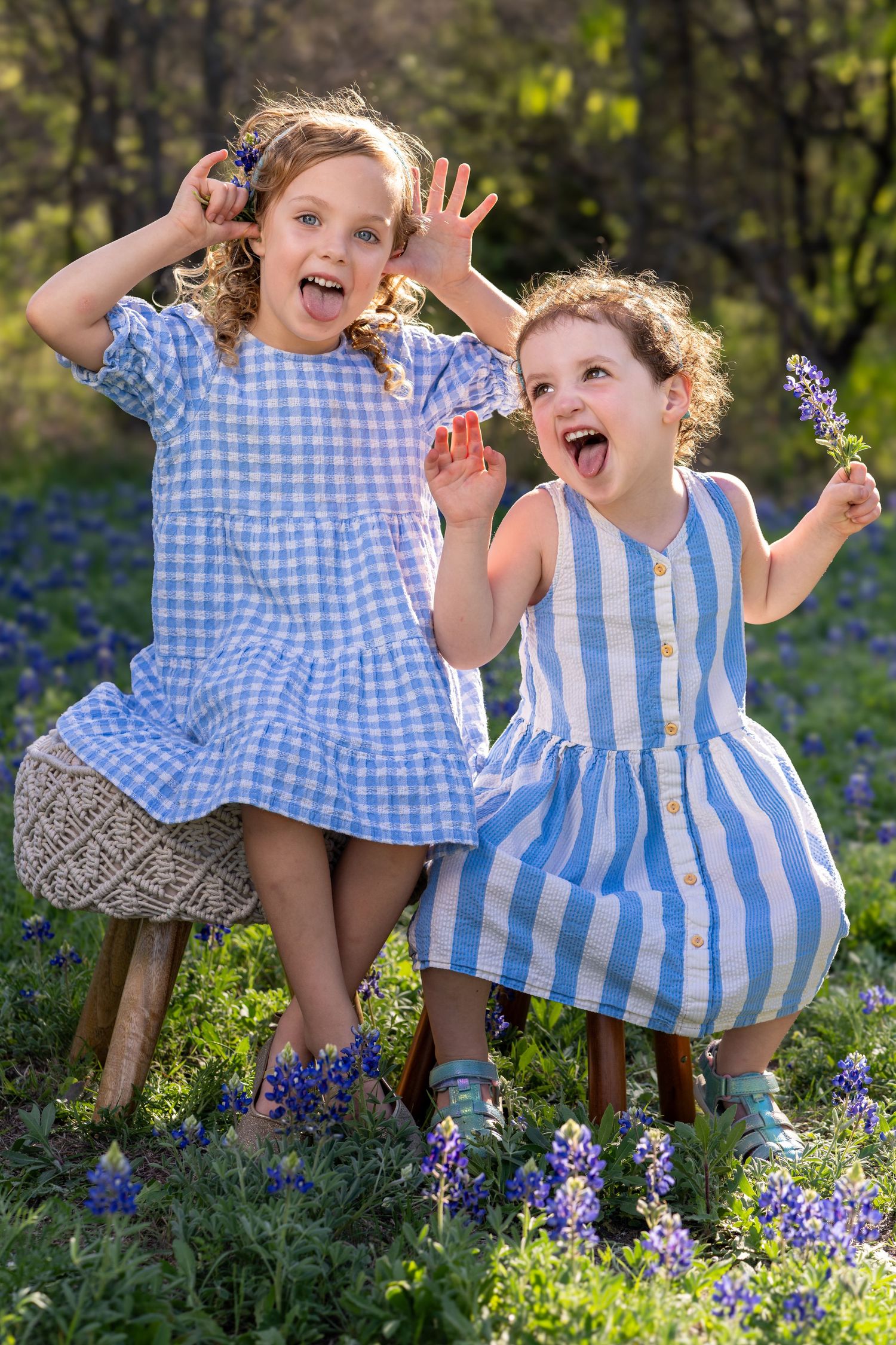 Two children in blue and white outfits play and laugh together among blooming spring flowers in a garden.