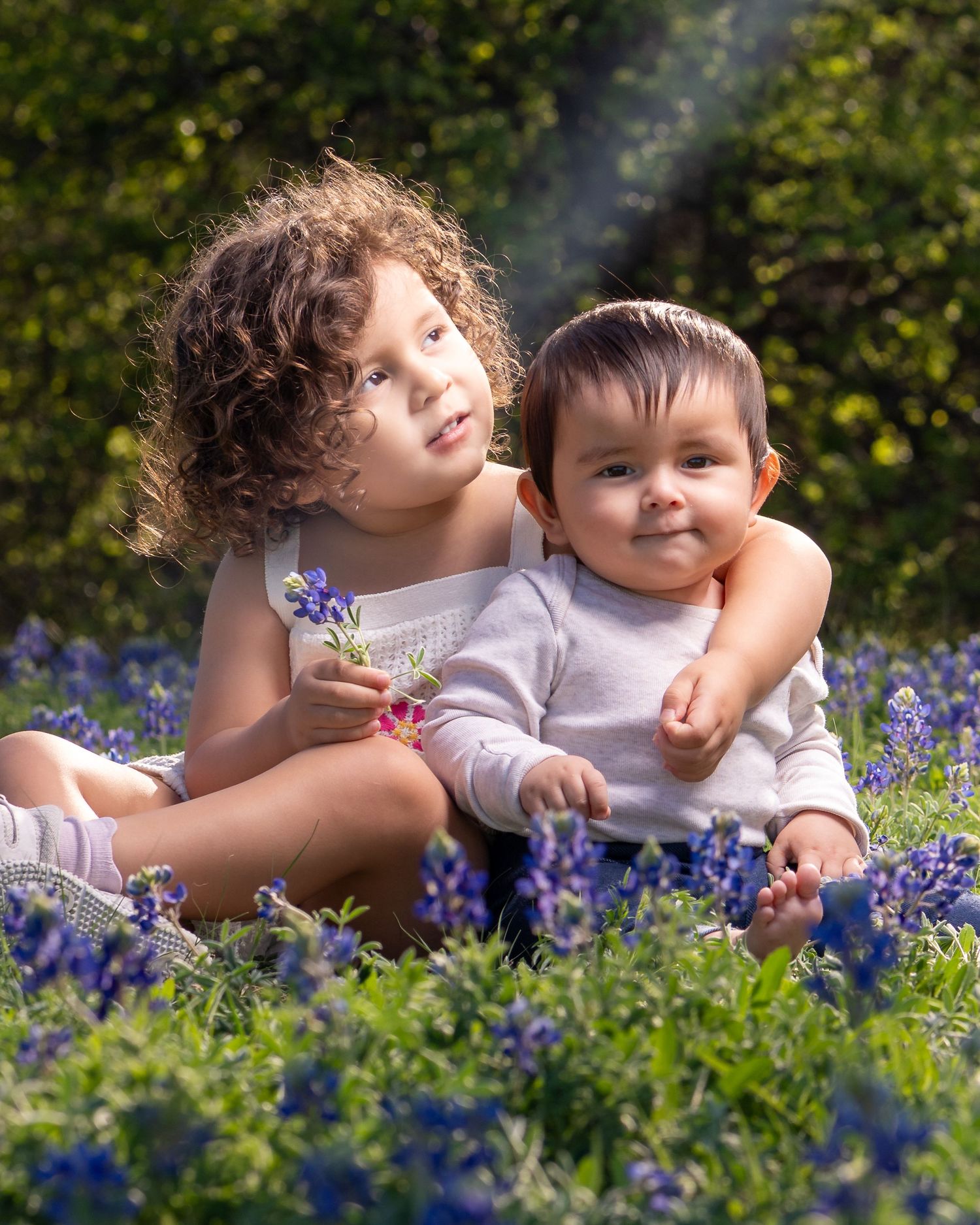 Two children pose together among blooming bluebonnets in a springtime outdoor portrait session.