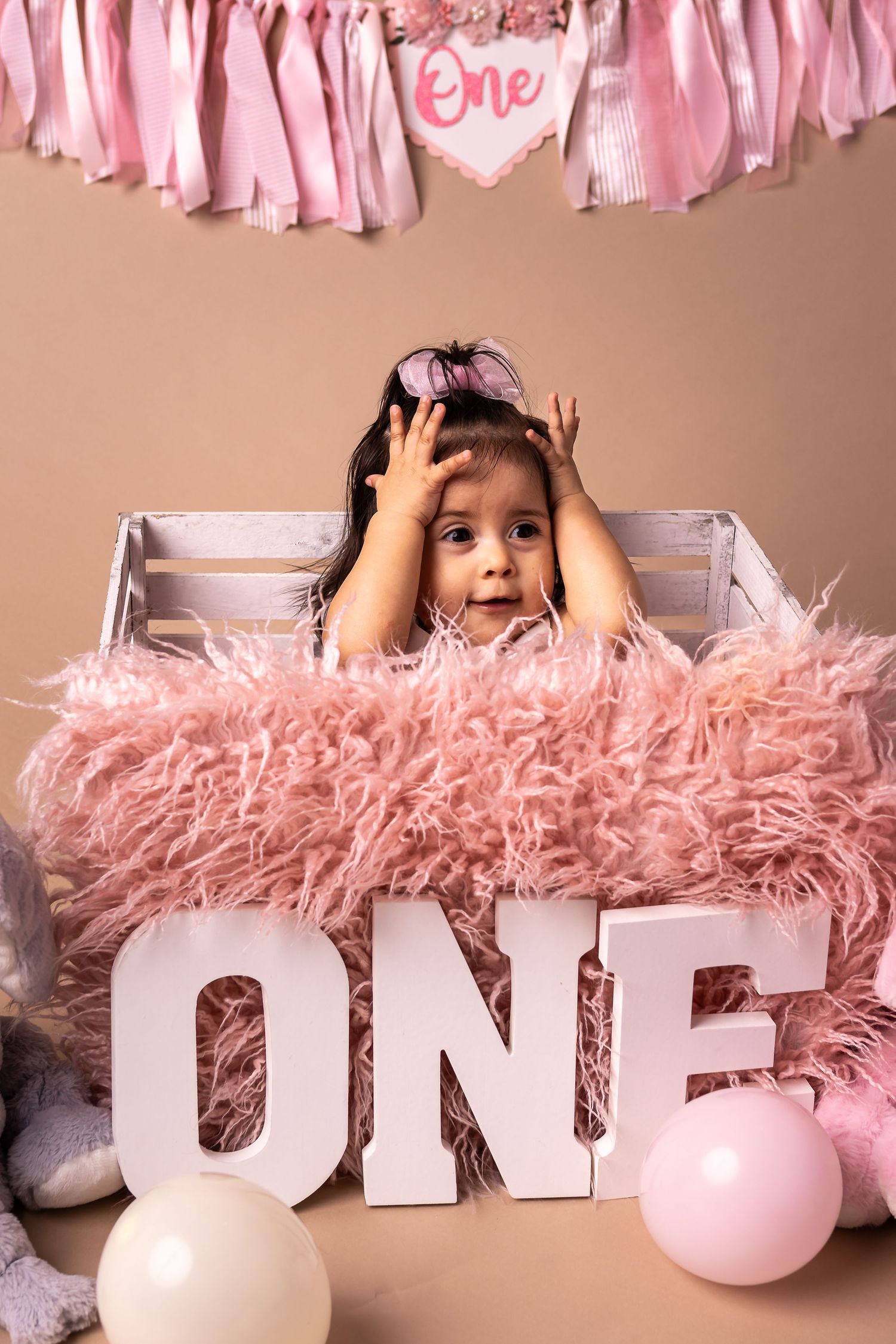 A pink and white first birthday photo setup with large white 'ONE' letters and fluffy pink decorations.