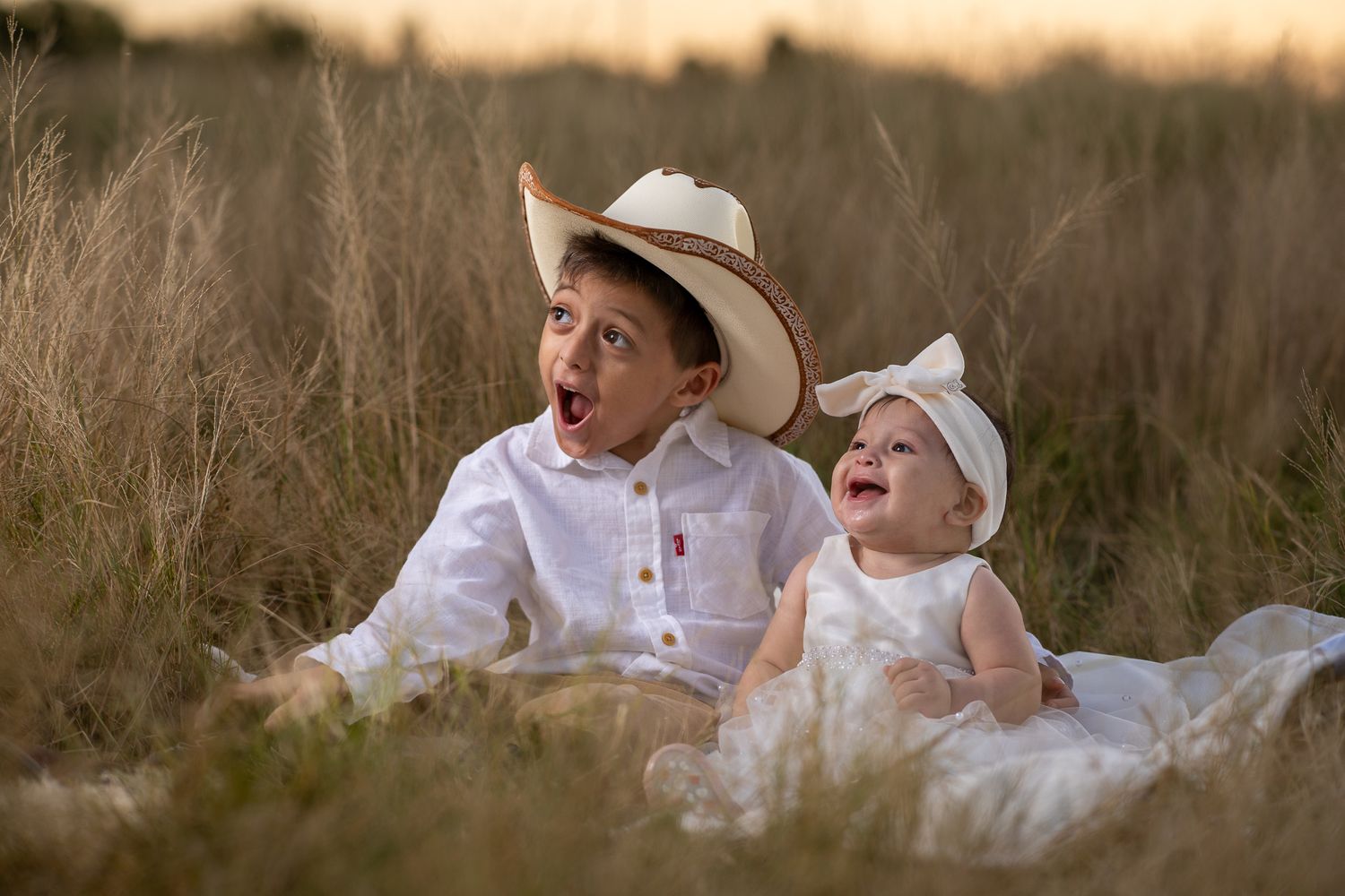 Two young children in white outfits playing together at sunset.