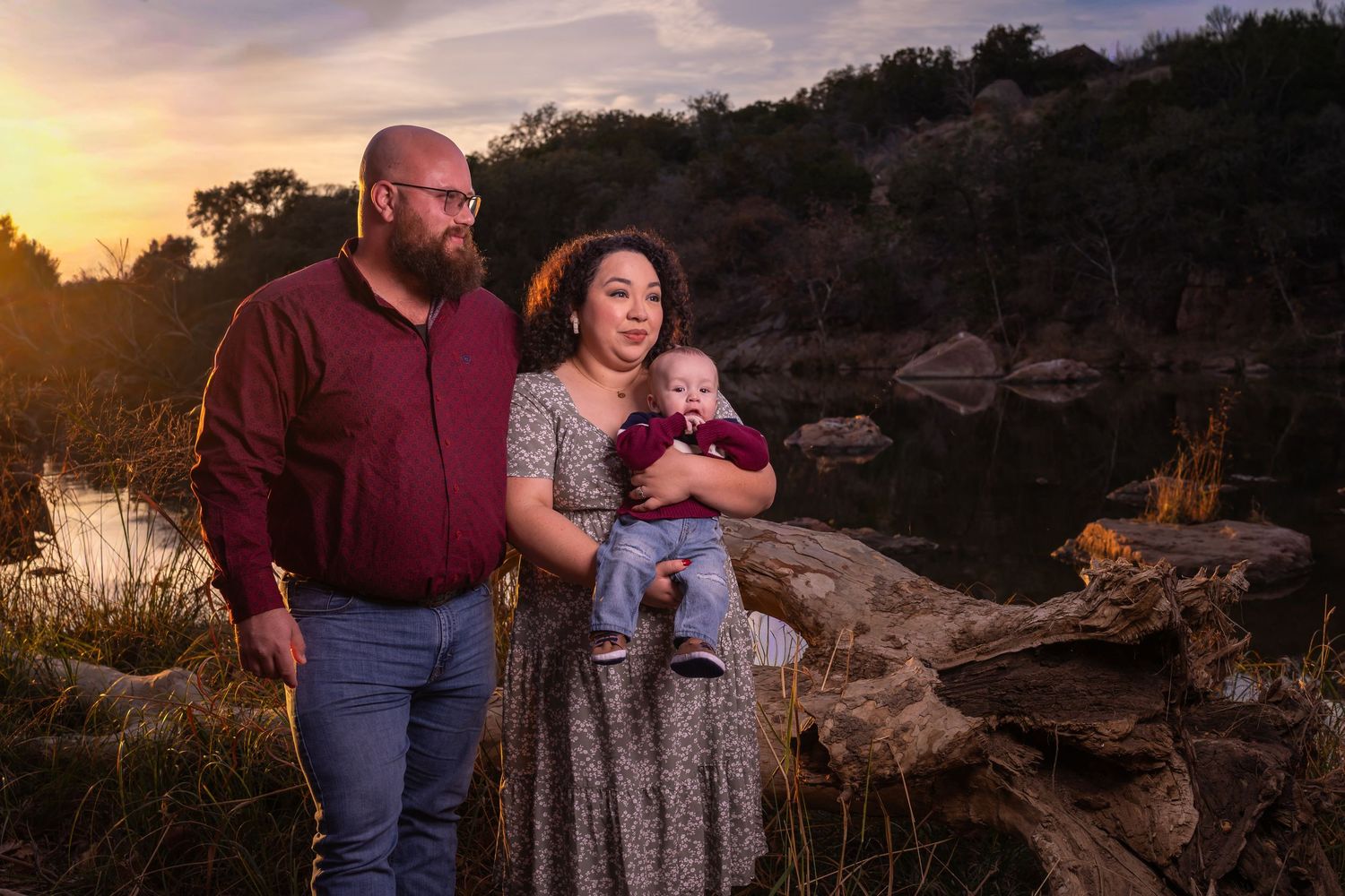 A couple in burgundy and gray outfits share tender moments during a sunset photoshoot among desert rocks and foliage.