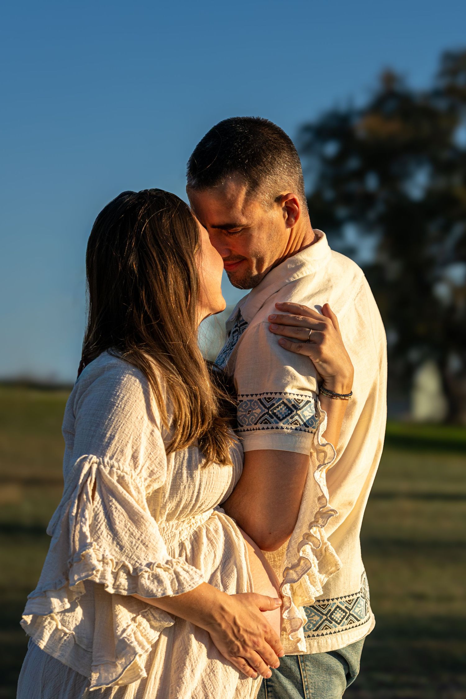 A couple embraces in a romantic sunset photoshoot series outdoors in a grassy field.