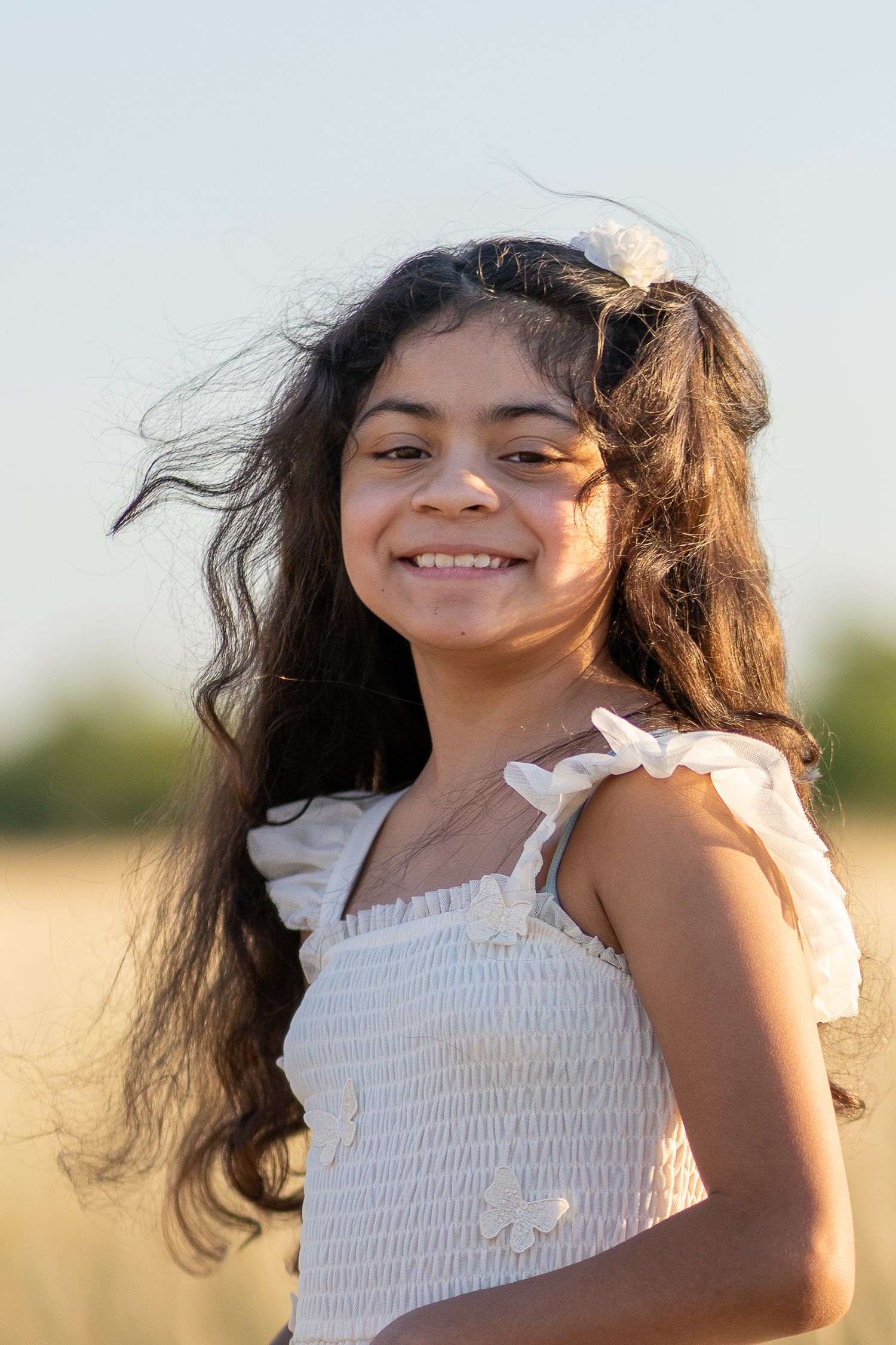 A series of photos showing someone with flowing dark hair wearing a white smocked dress in a sunlit outdoor setting.