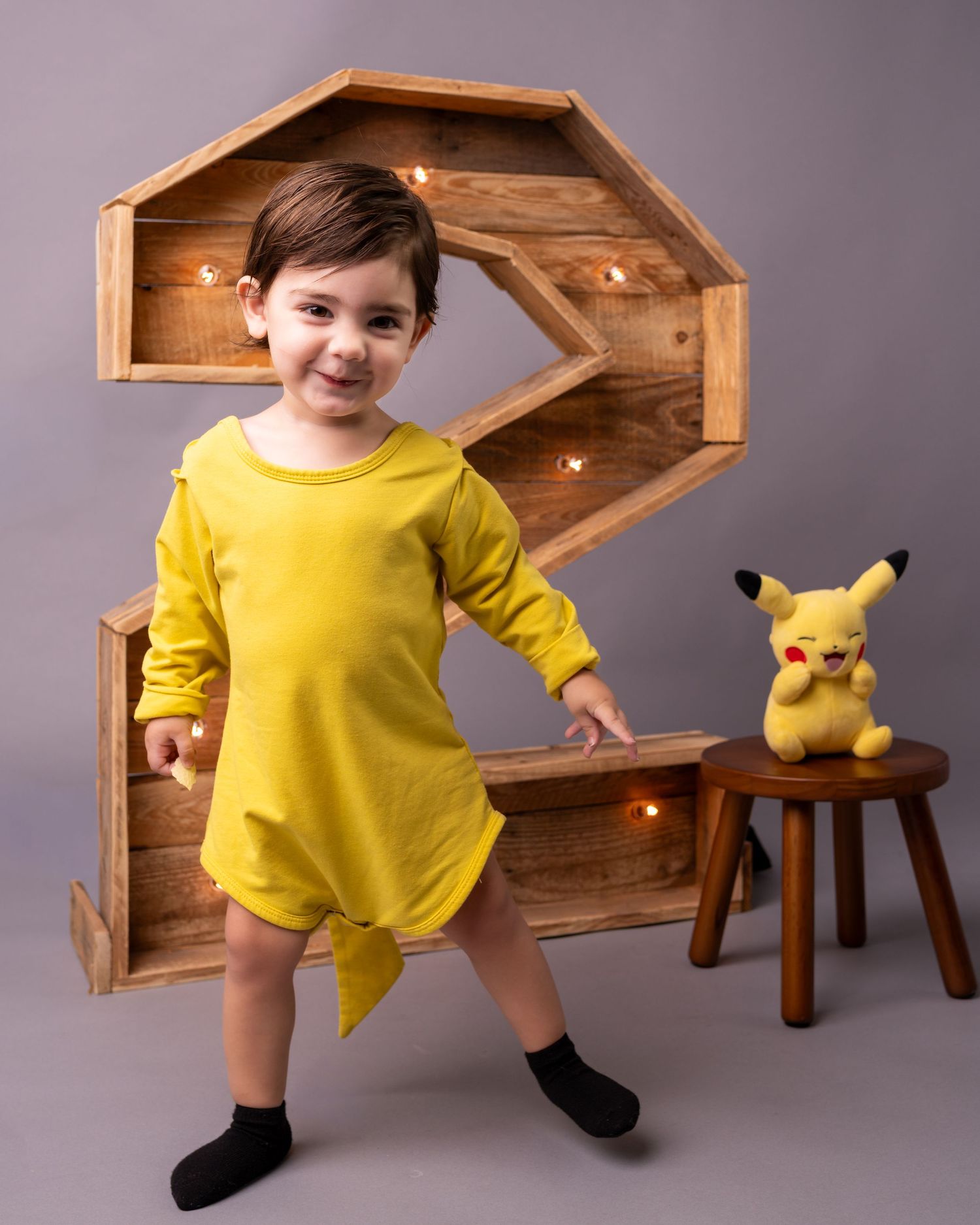 A bright yellow dress against a wooden display with a Pikachu plush toy sitting on a small stool.