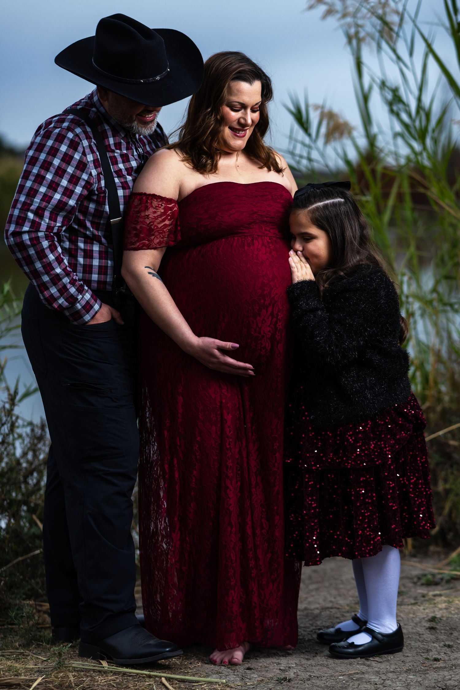 A family in burgundy dress and plaid shirt poses together by a lakeside in a sequence of candid moments.