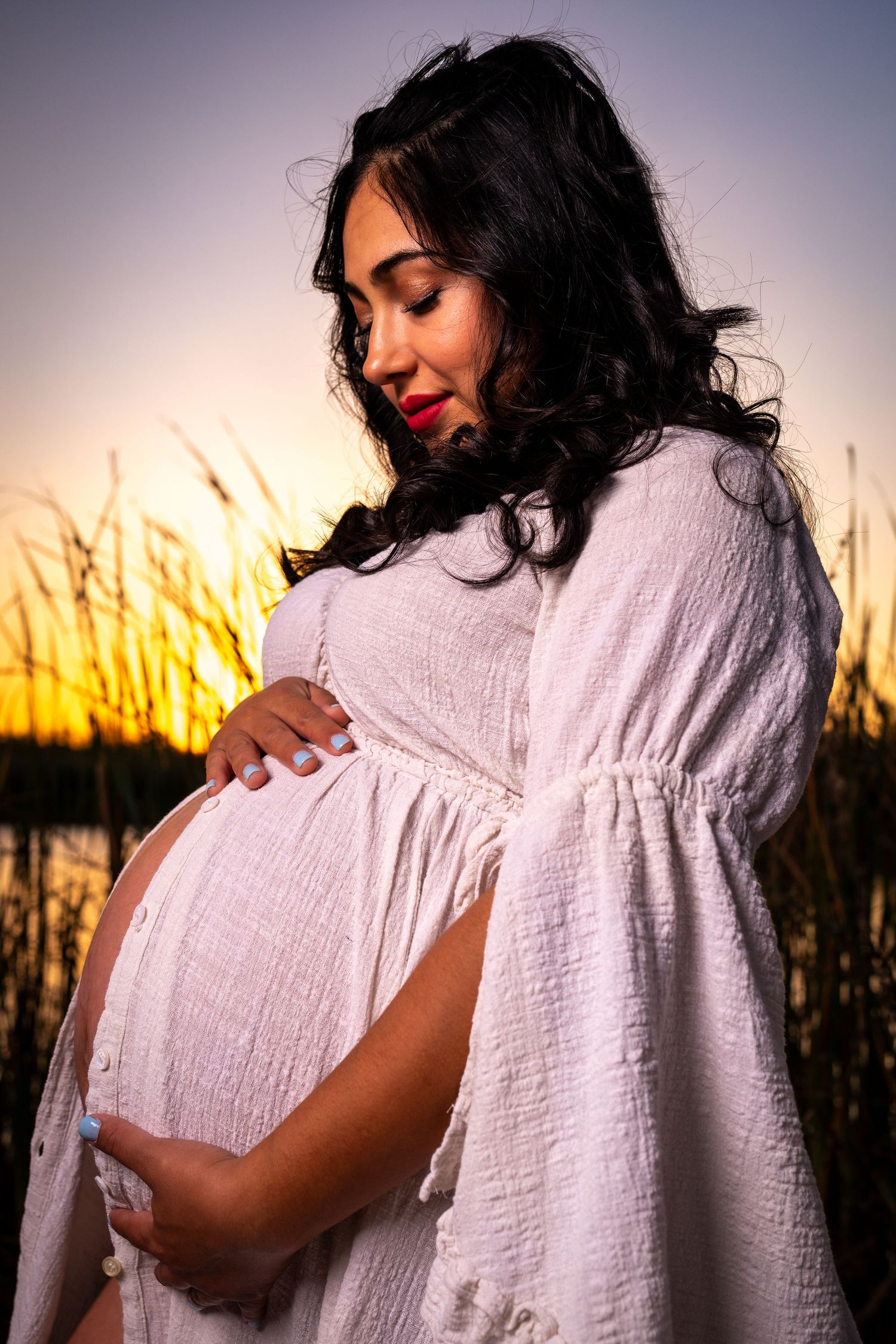 A pregnant woman in a white dress poses during golden hour sunset in a series of silhouetted maternity photos.