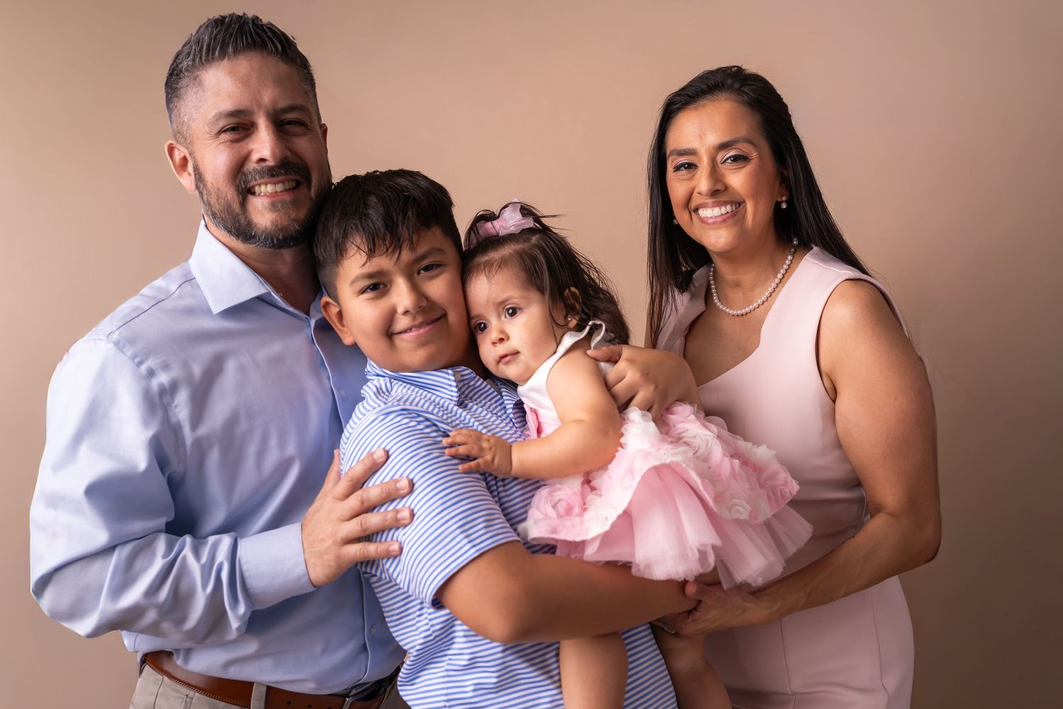 A family wearing coordinated neutral tones embraces and laughs together during a professional photo session.