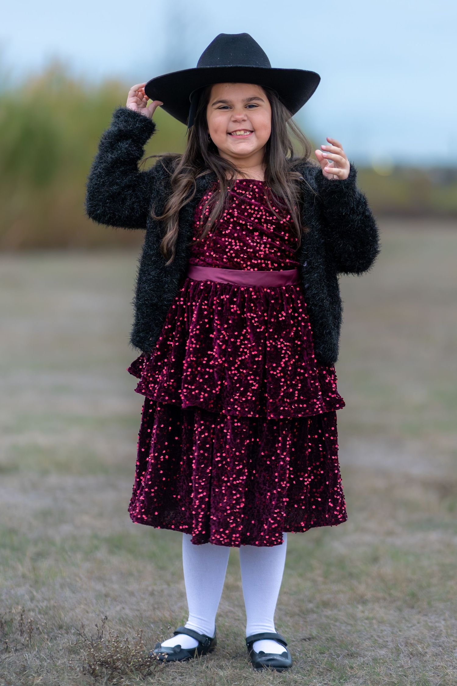 A sparkly burgundy velvet dress paired with white tights and a black hat creates a festive holiday outfit.