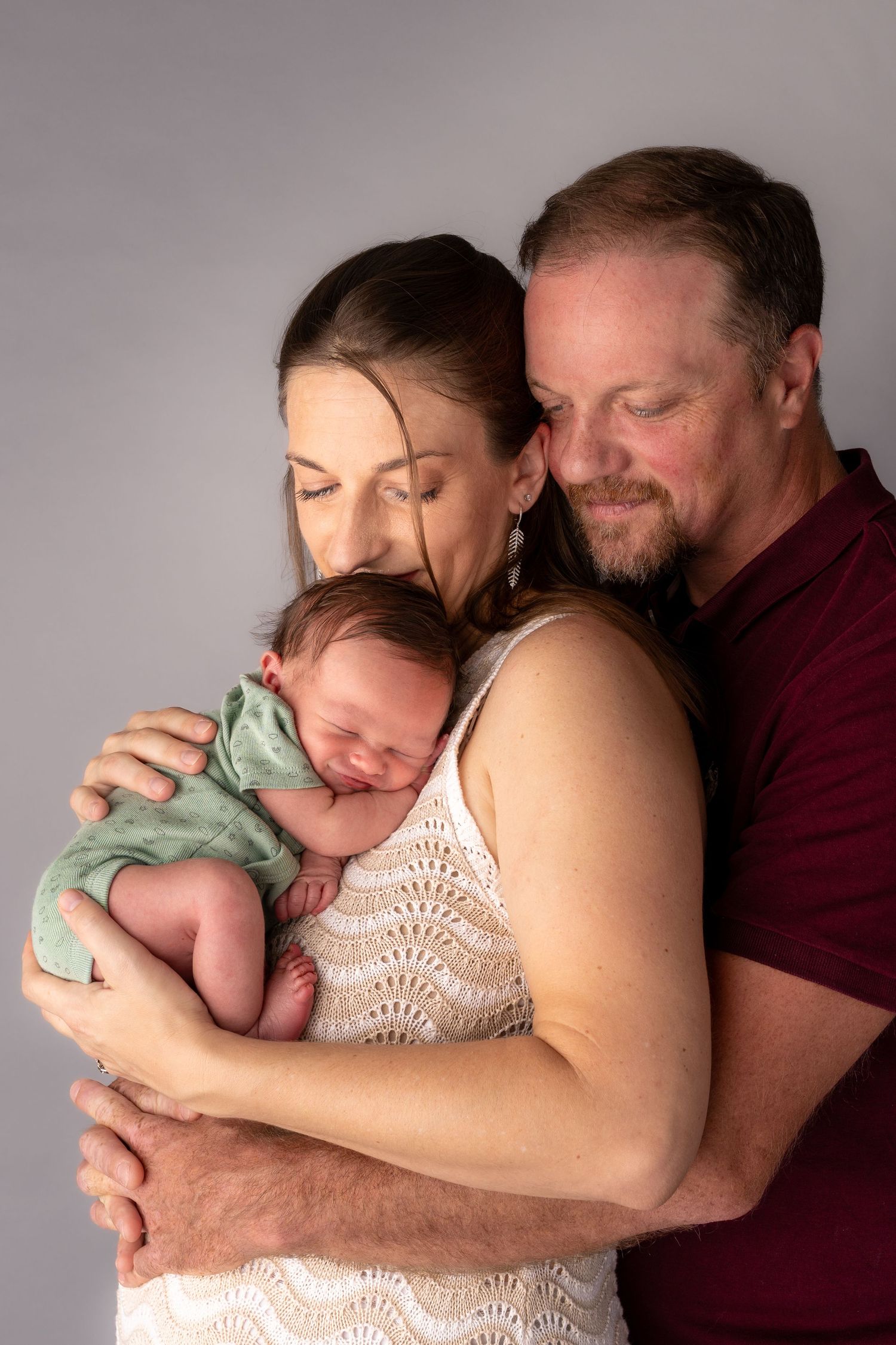 Parents tenderly hold their sleeping newborn baby wrapped in green during a studio portrait session.