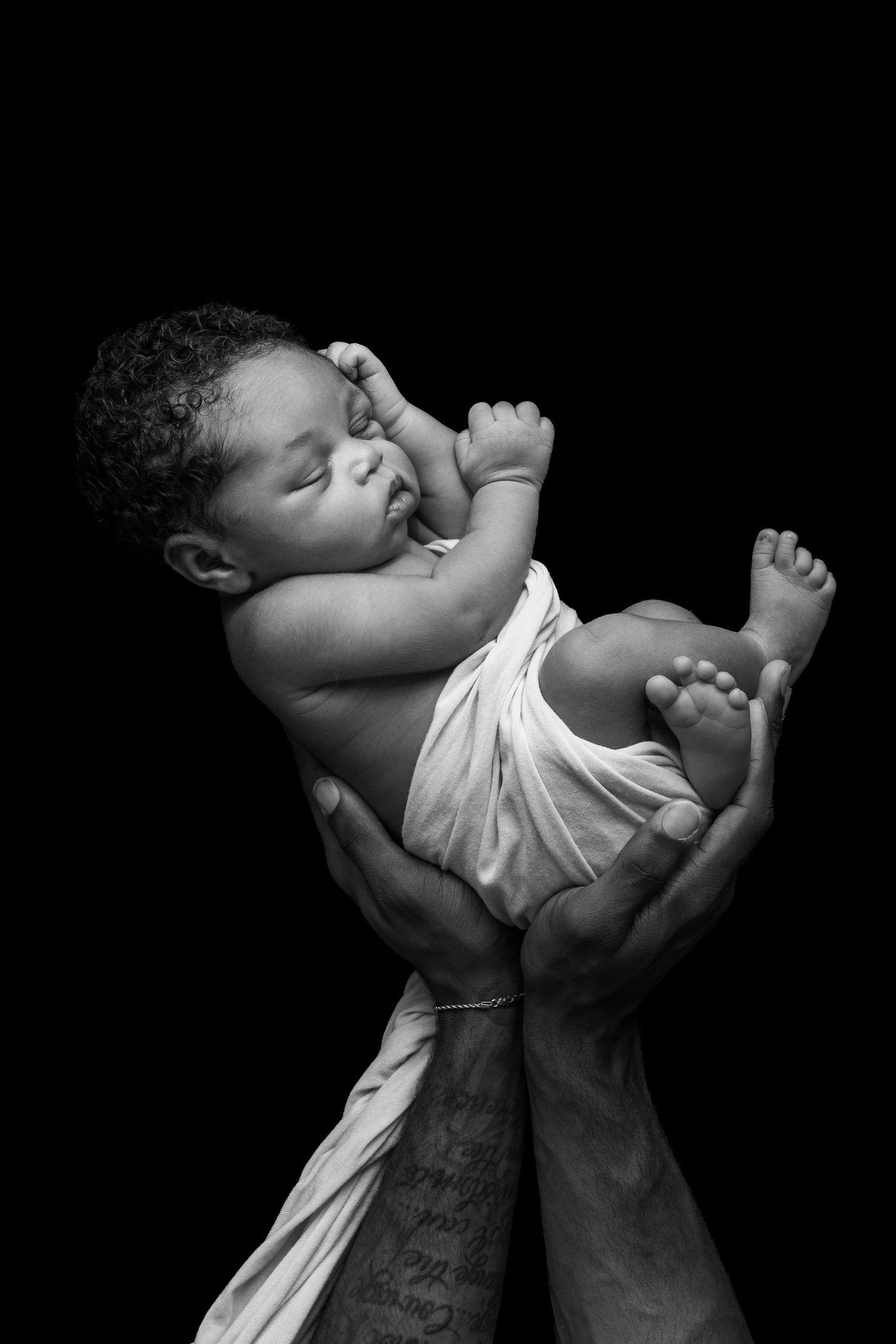 Black and white photo of a sleeping newborn baby cradled in adult hands against a dark background.