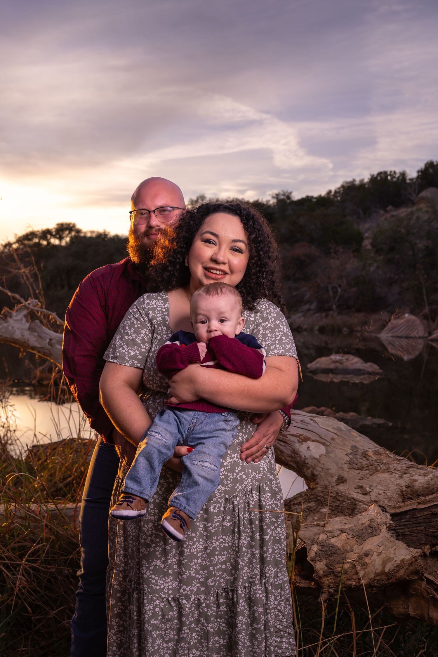 Family embraces together during sunset photoshoot at rocky outdoor location with warm golden lighting.