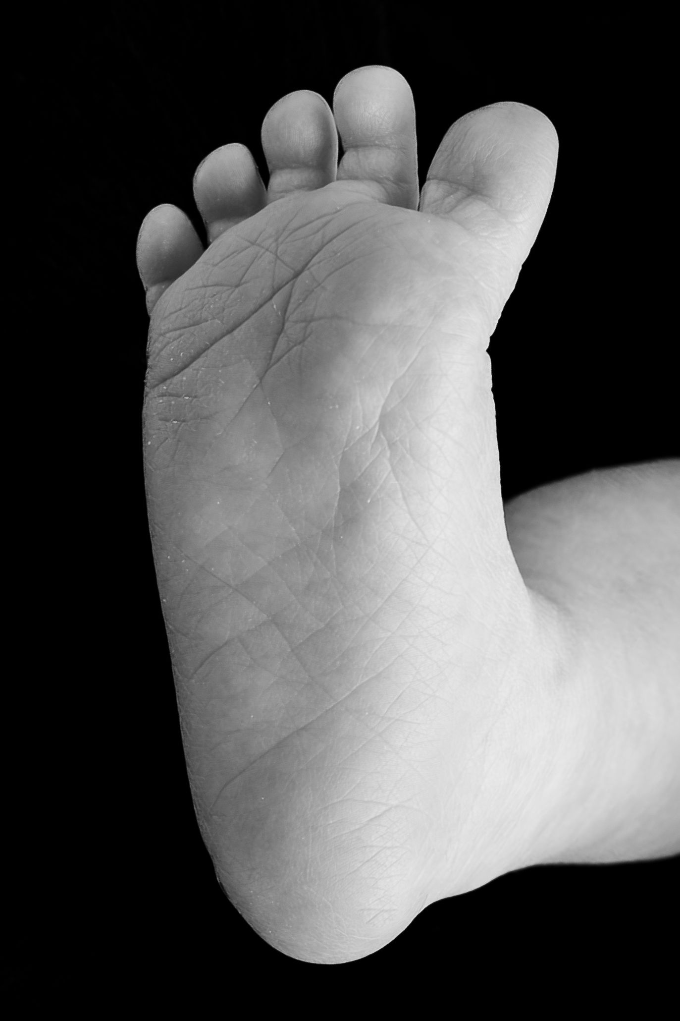 Black and white close-up photo of a baby's foot sole against a dark background.