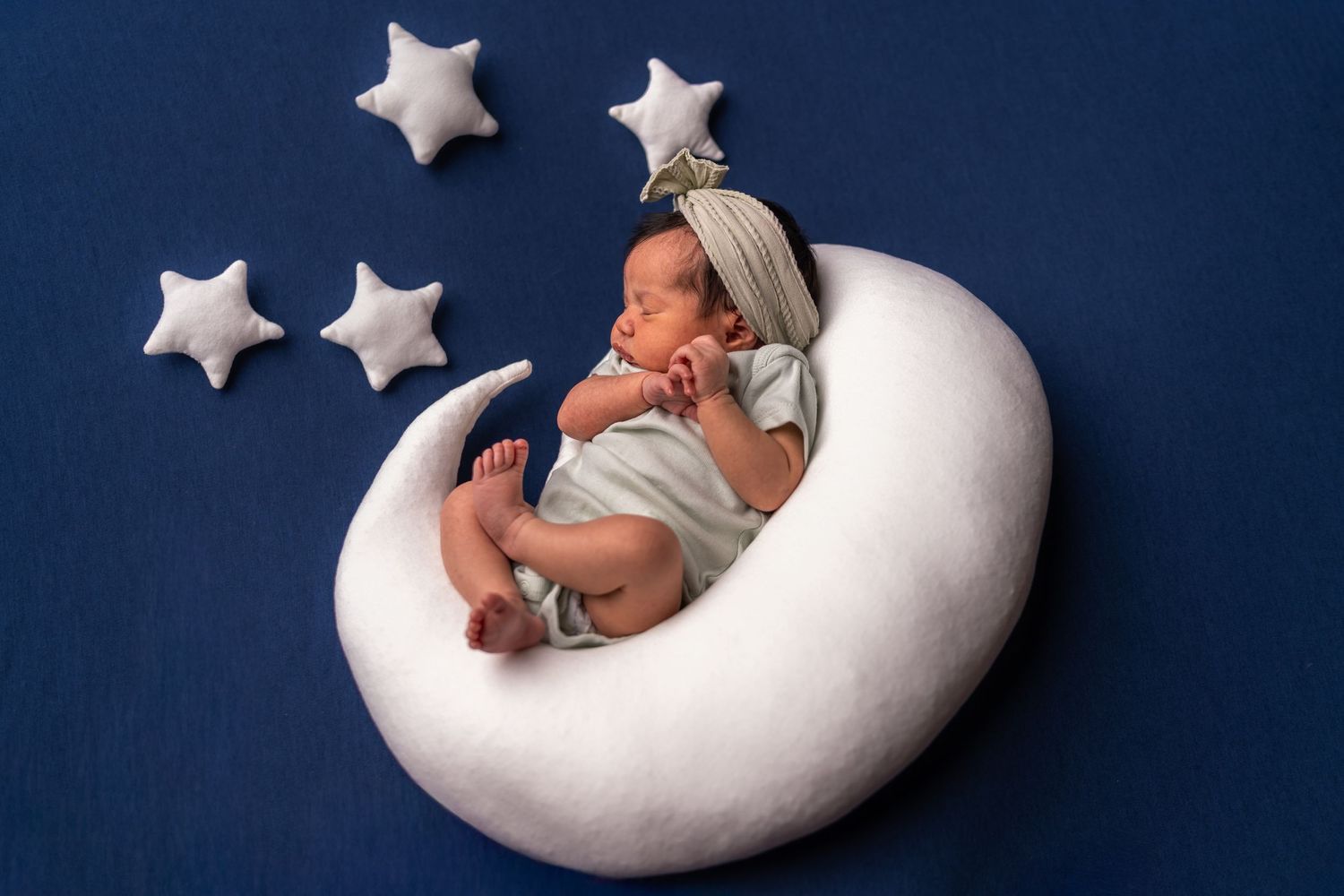 A series of photos showing a newborn baby posed on white crescent moon and star props against a dark blue background.