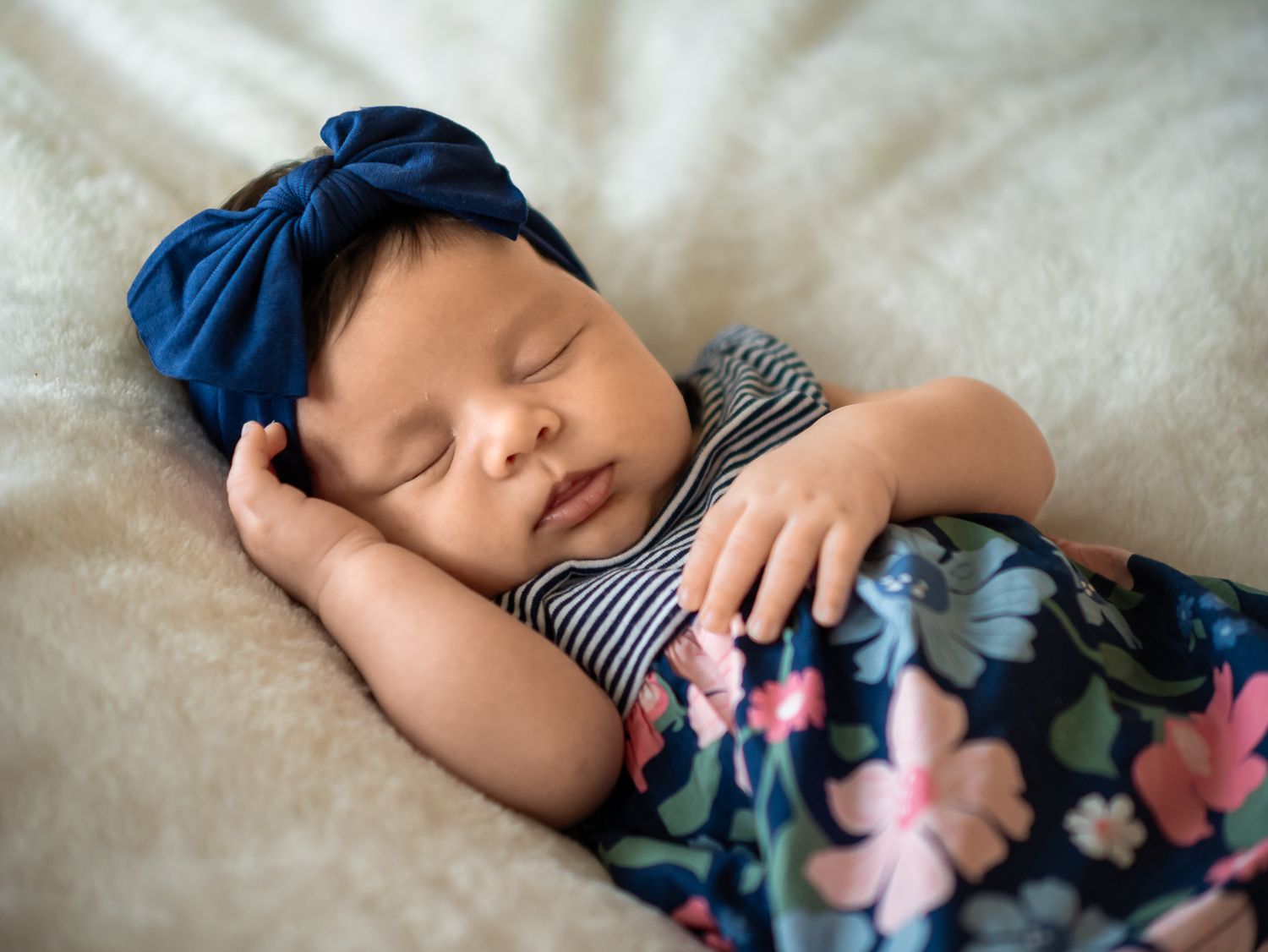 Newborn photograph of baby girl sleeping peacefully with floral decorations on white bedding in Buda.
