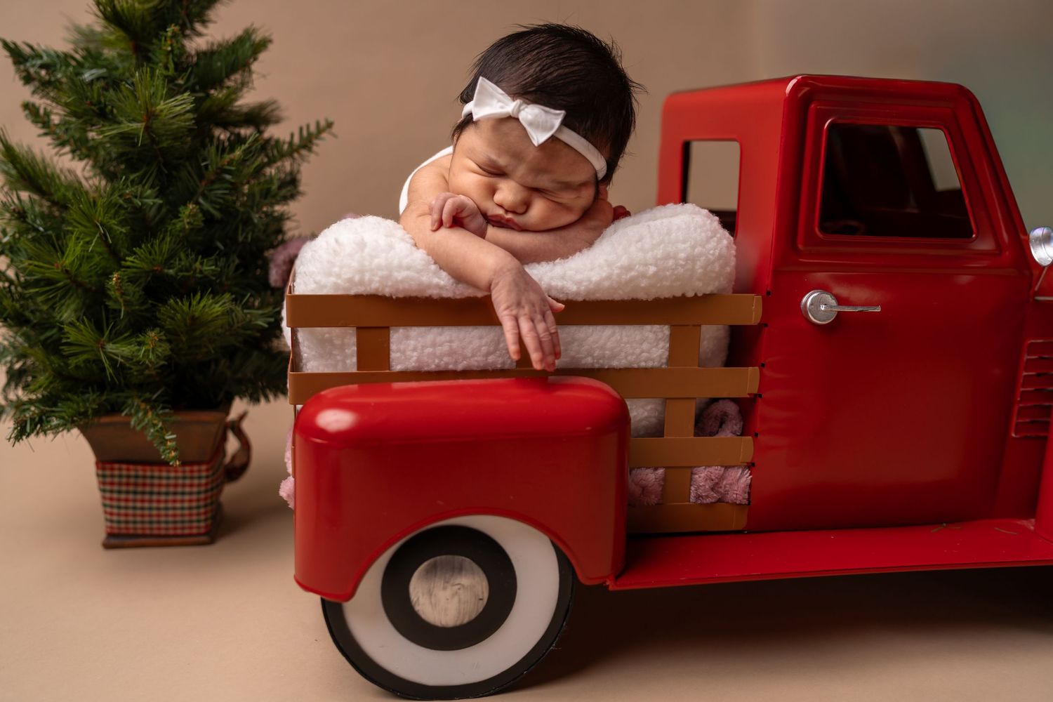 Newborn sleeps inside the bed of a vintage red pickup truck with classic white-wall tires during Christmastime in Sunfield, Buda TX.