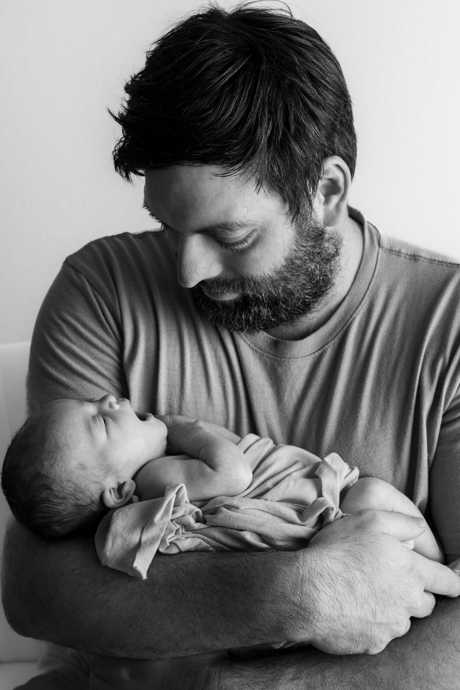 Black and white photo of a bearded father tenderly holding his sleeping newborn baby in his arms.