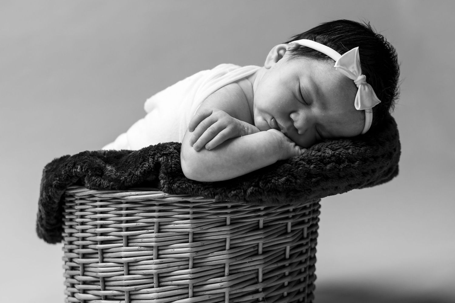 Black and white photograph of a sleeping baby nestled in a woven basket.