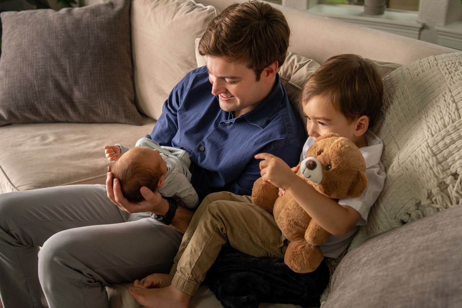 Two young boys sitting on couch together playing with teddy bears at home.