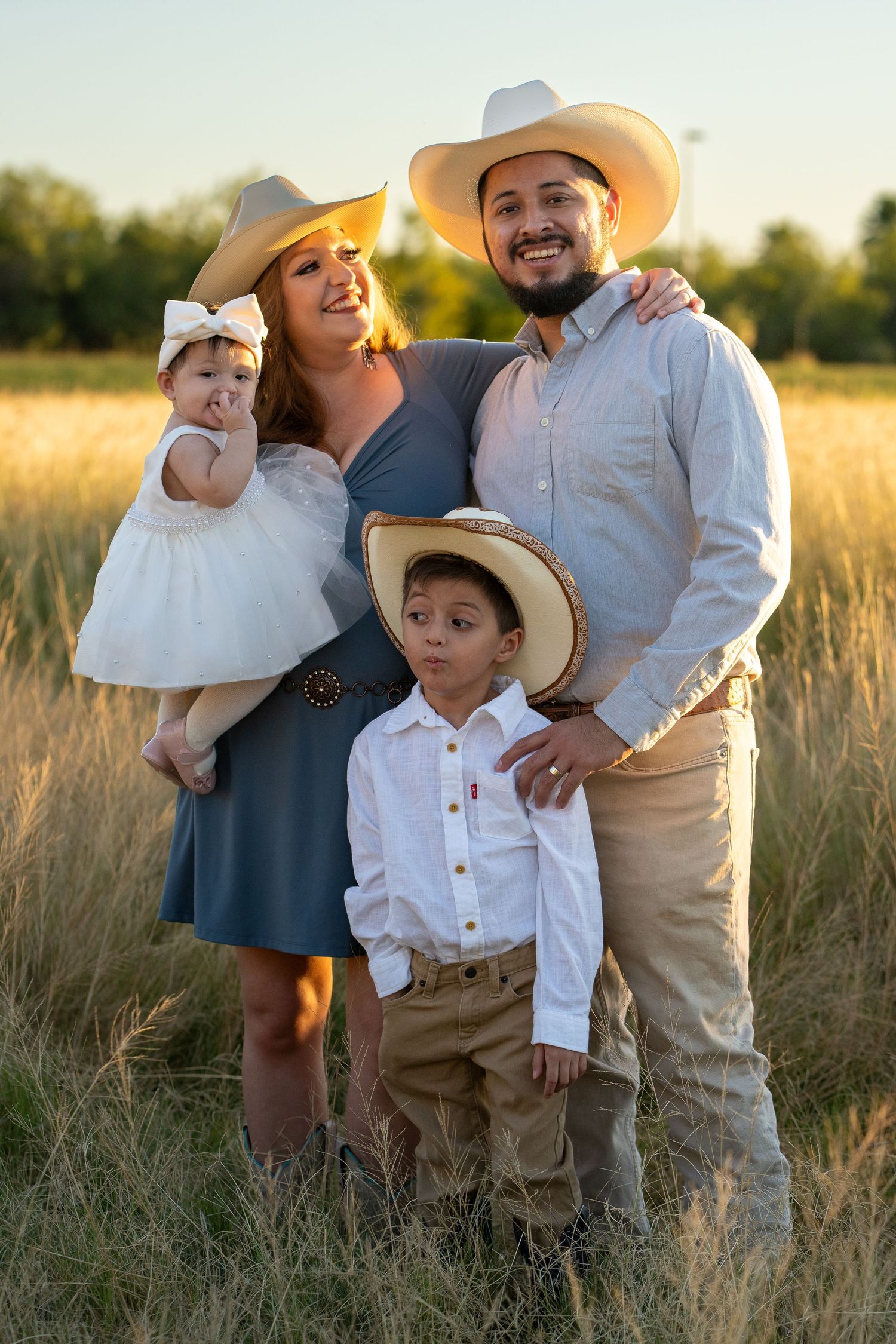 Family in western attire poses together in a golden sunlit field during sunset.