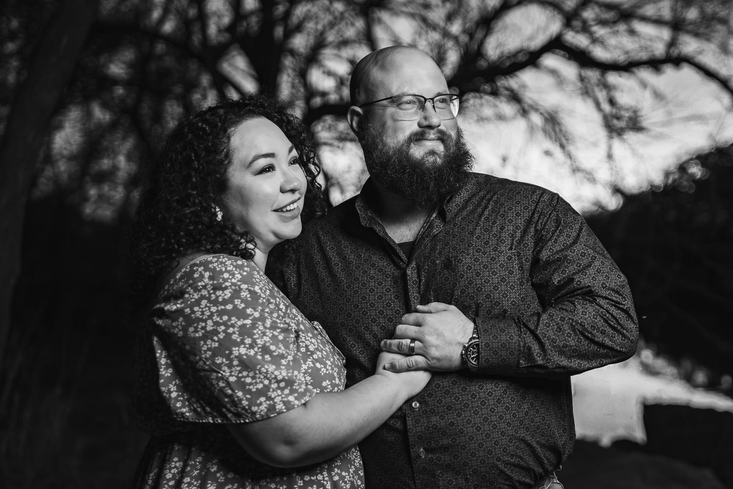 A couple in formal attire embraces outdoors during a romantic photo session at sunset.