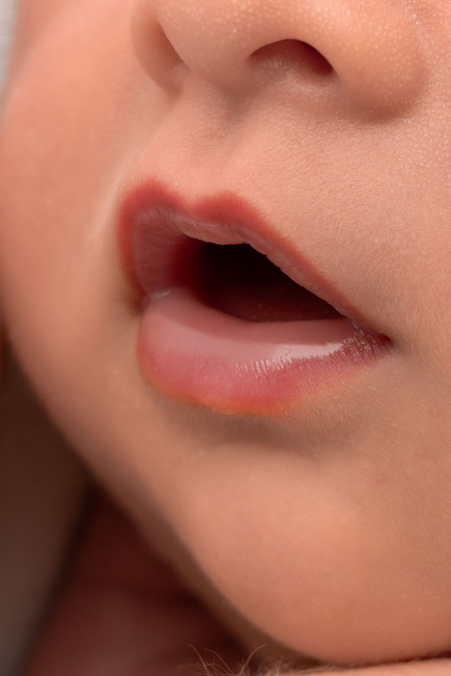 Macro shot of a newborn baby's lips and nose, slightly open mouth.